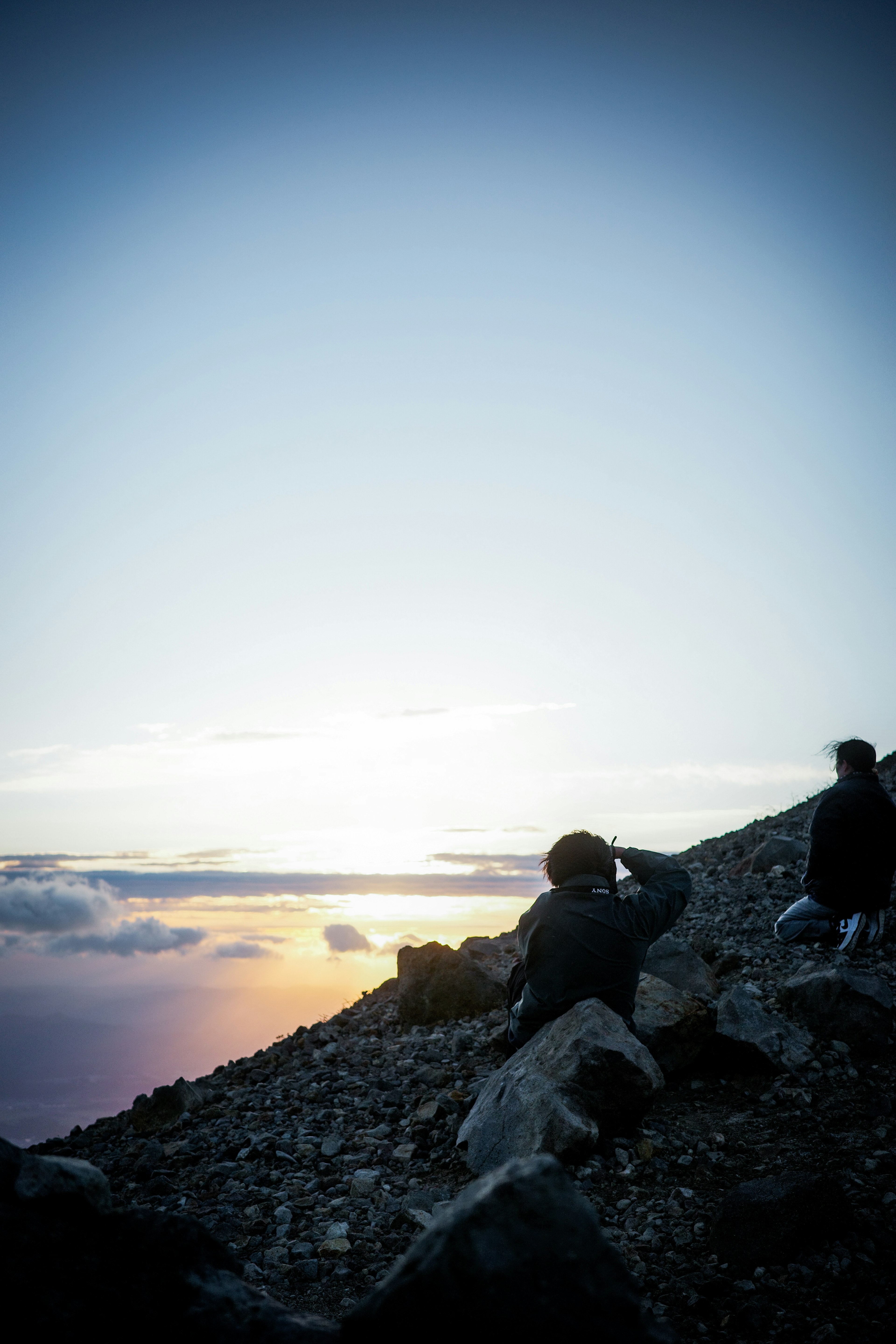 夕日を背にした登山者たちが岩の上に座っている