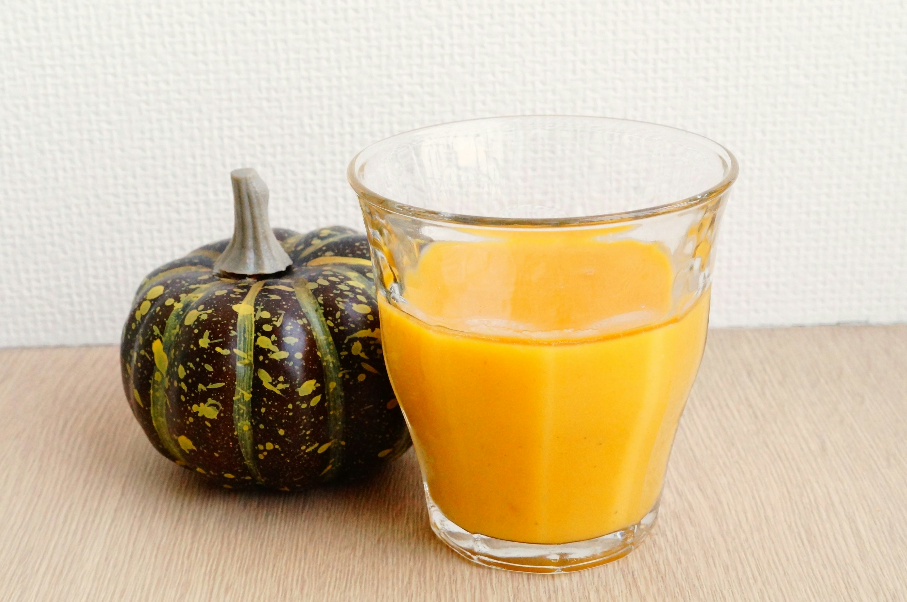 Un vaso de bebida naranja al lado de una calabaza verde