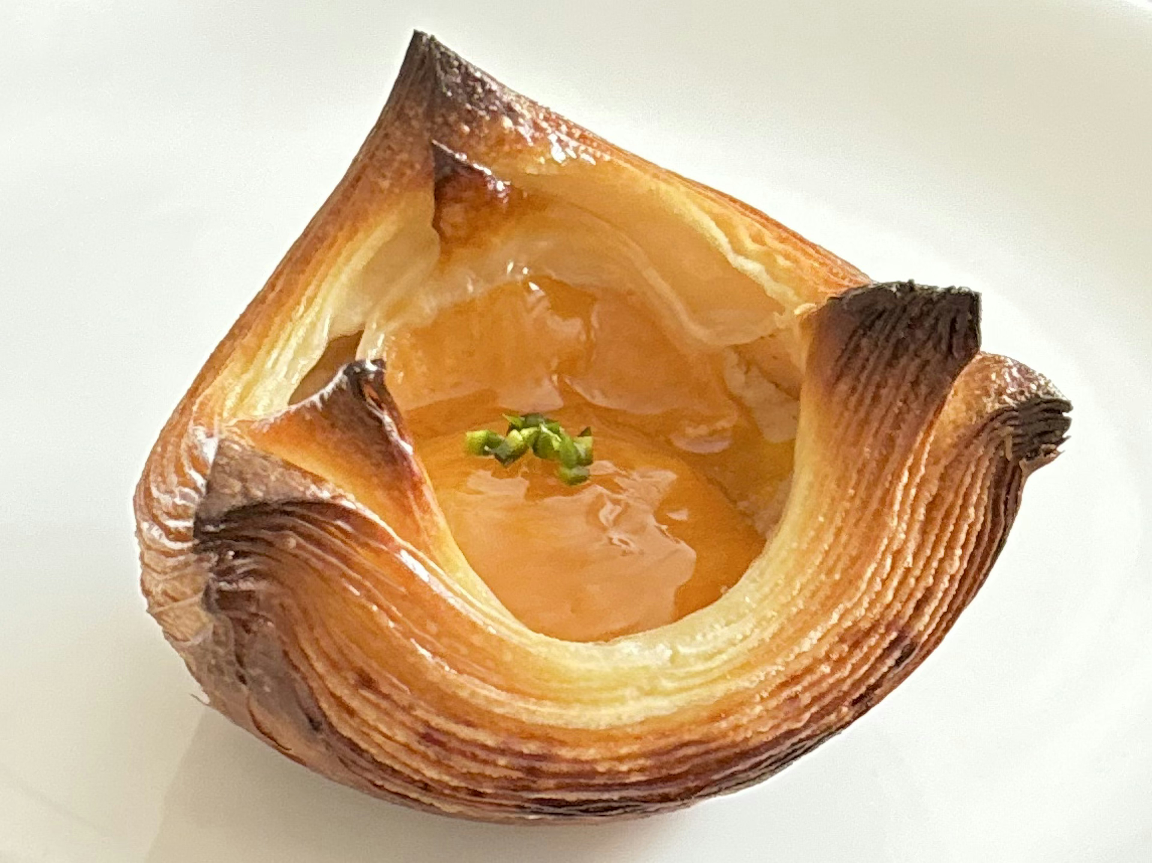 A beautifully caramelized pastry with a glossy center filled with transparent jelly and topped with green herbs