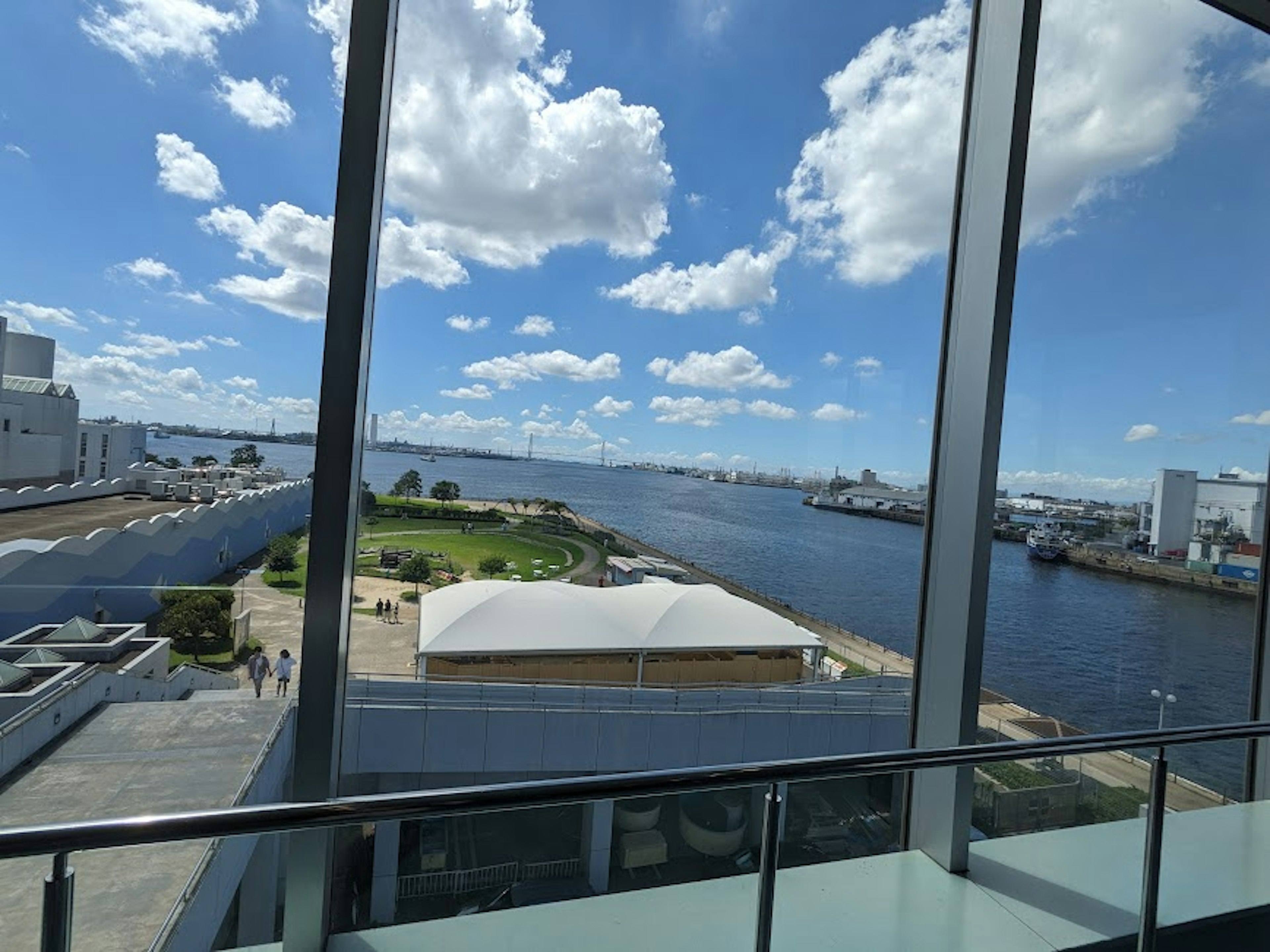 Vista de un río y cielo azul a través de ventanas de vidrio con vegetación y edificios