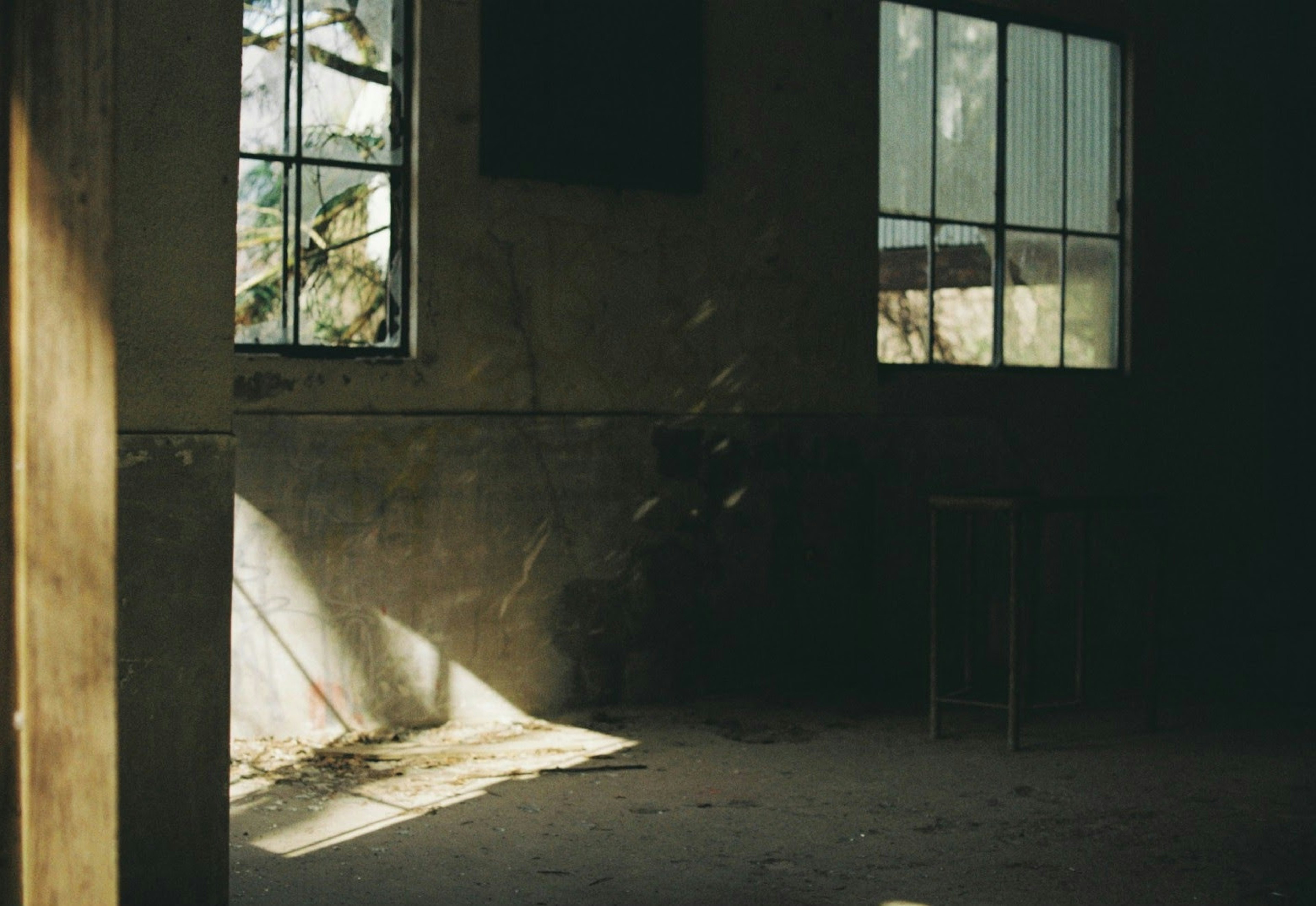 Habitación abandonada con luz solar que entra por las ventanas proyectando sombras en el suelo