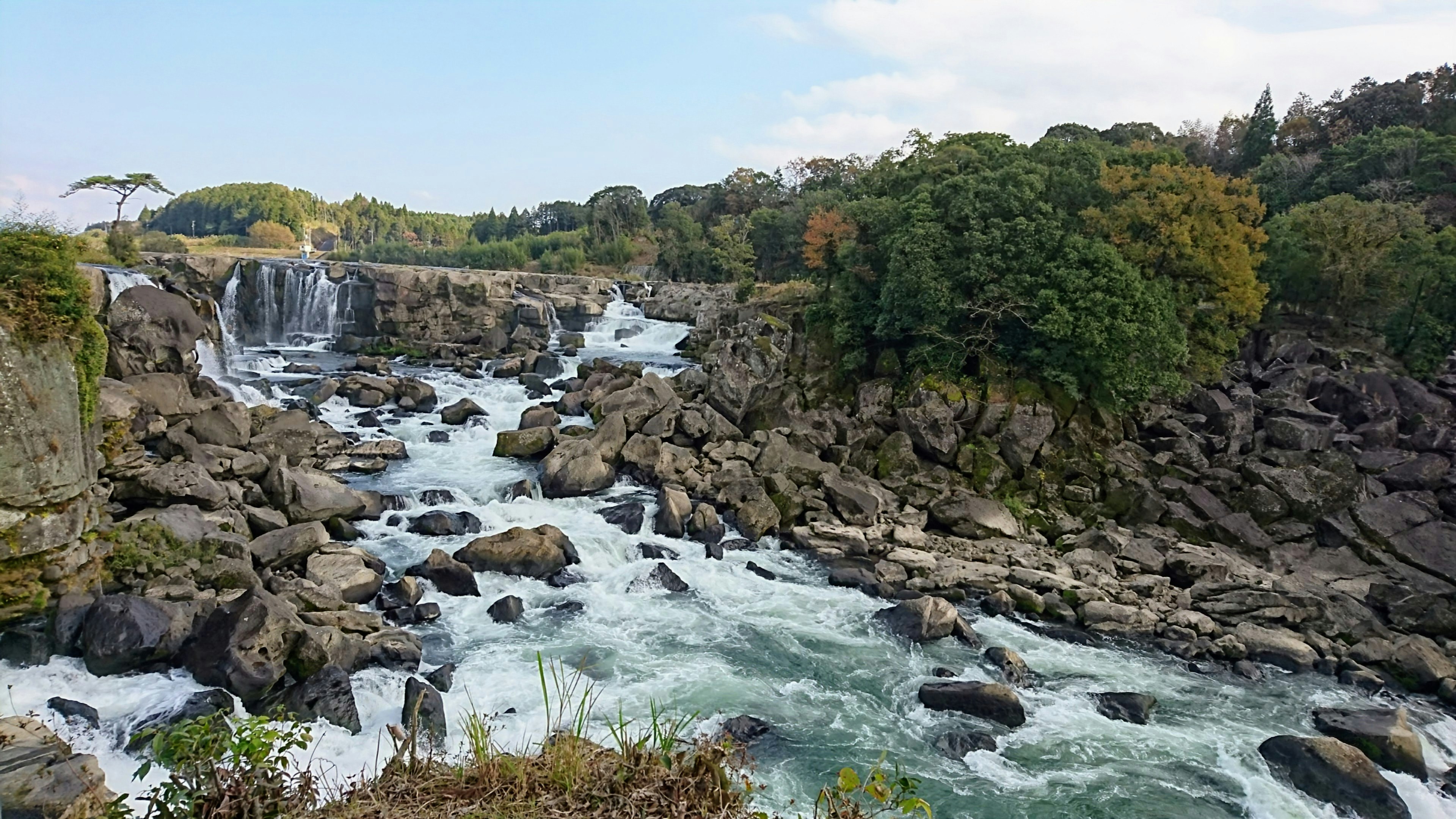 Vista panoramica di una cascata con rocce circondate da vegetazione lussureggiante e acqua che scorre