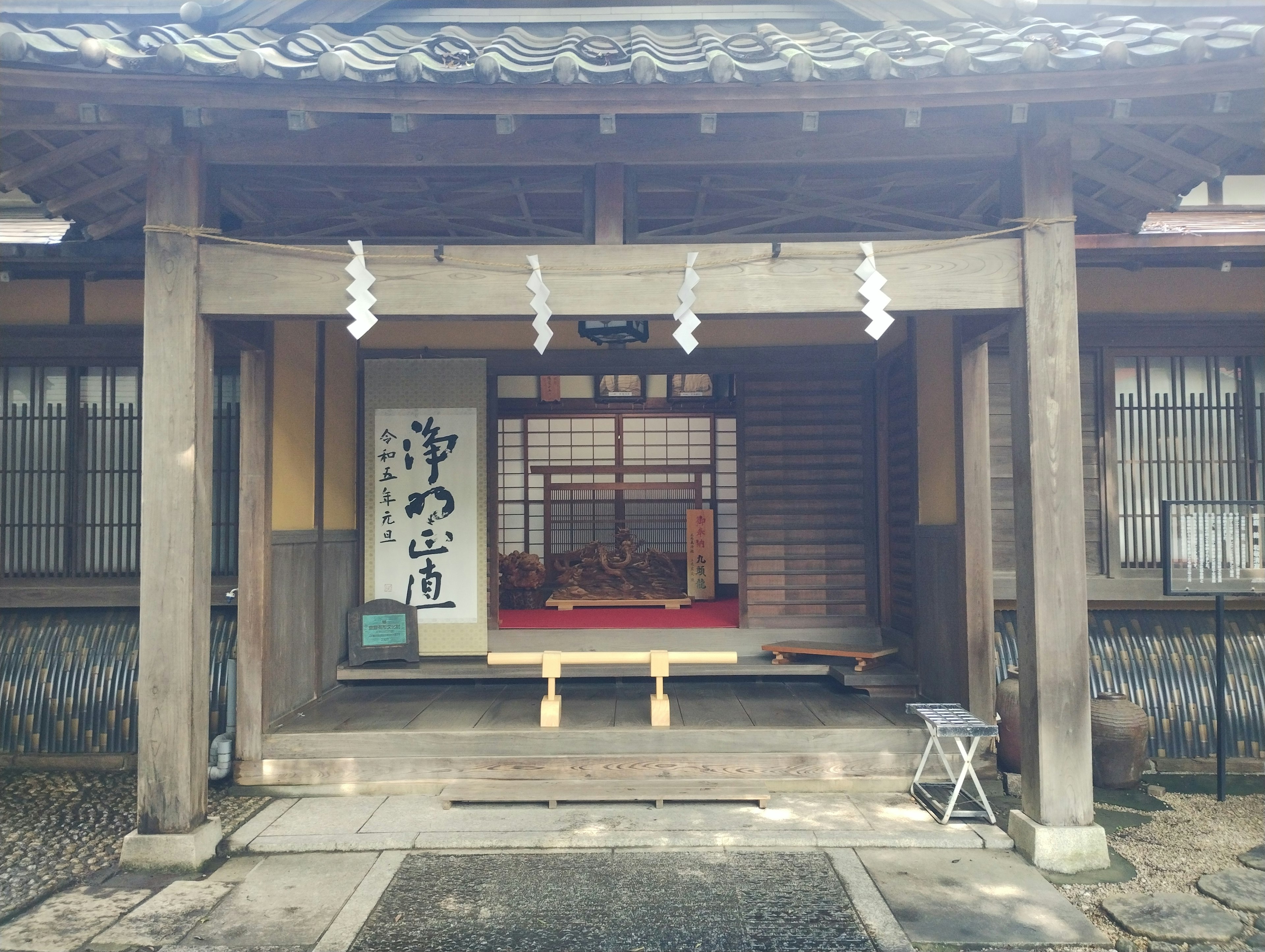 Entrance of a traditional Japanese house featuring wooden pillars and a roof with visible red tatami inside