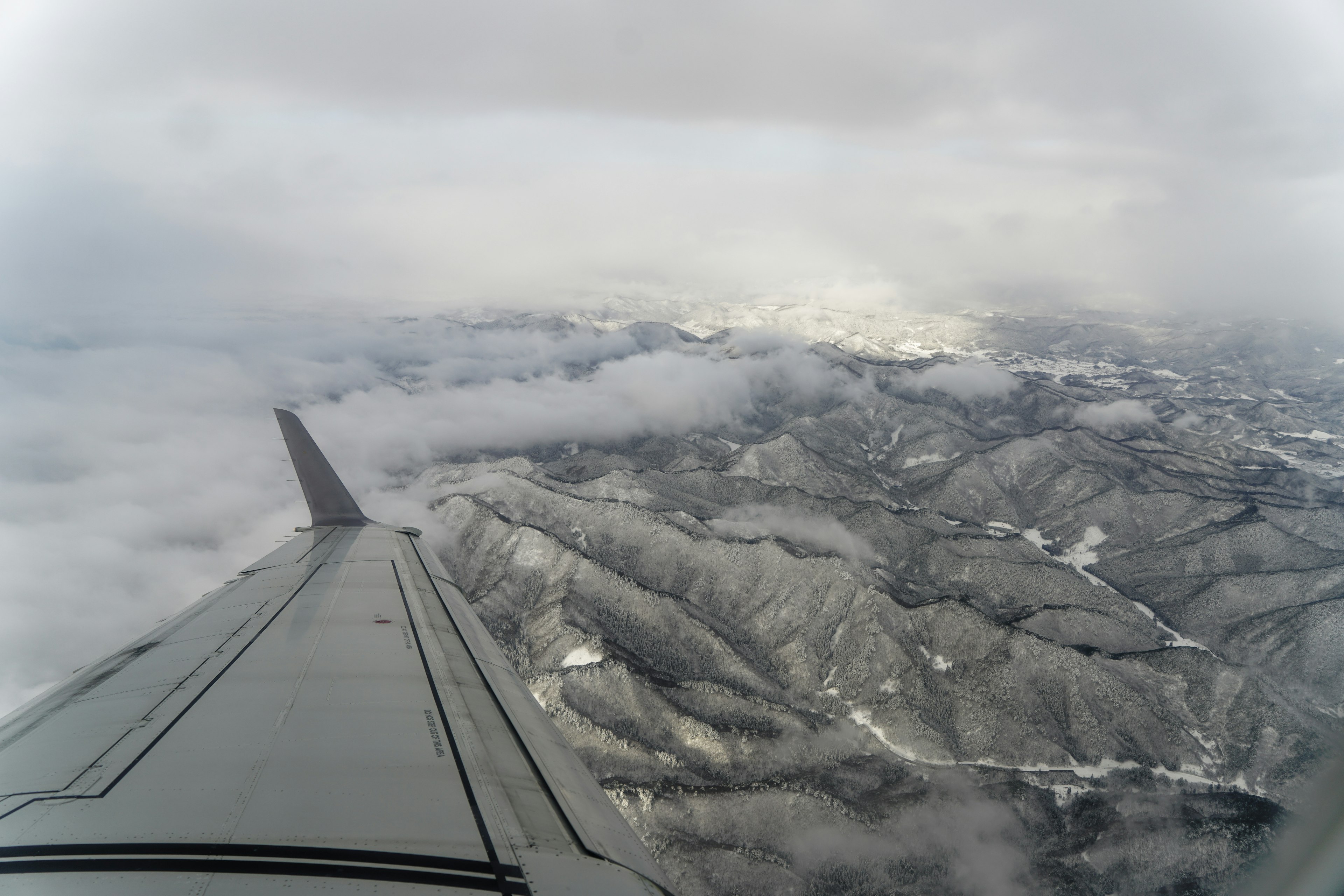 飛行機の翼から見た雪に覆われた山々と雲の景色