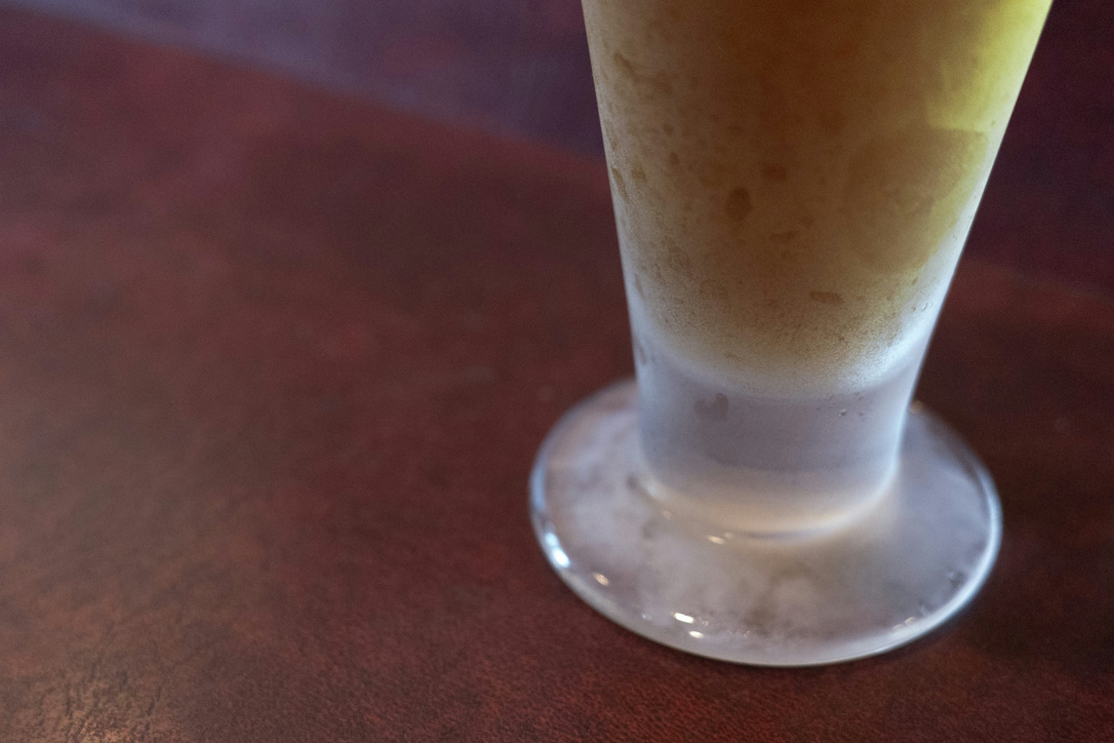 Partial view of a transparent glass with a drink on a wooden table