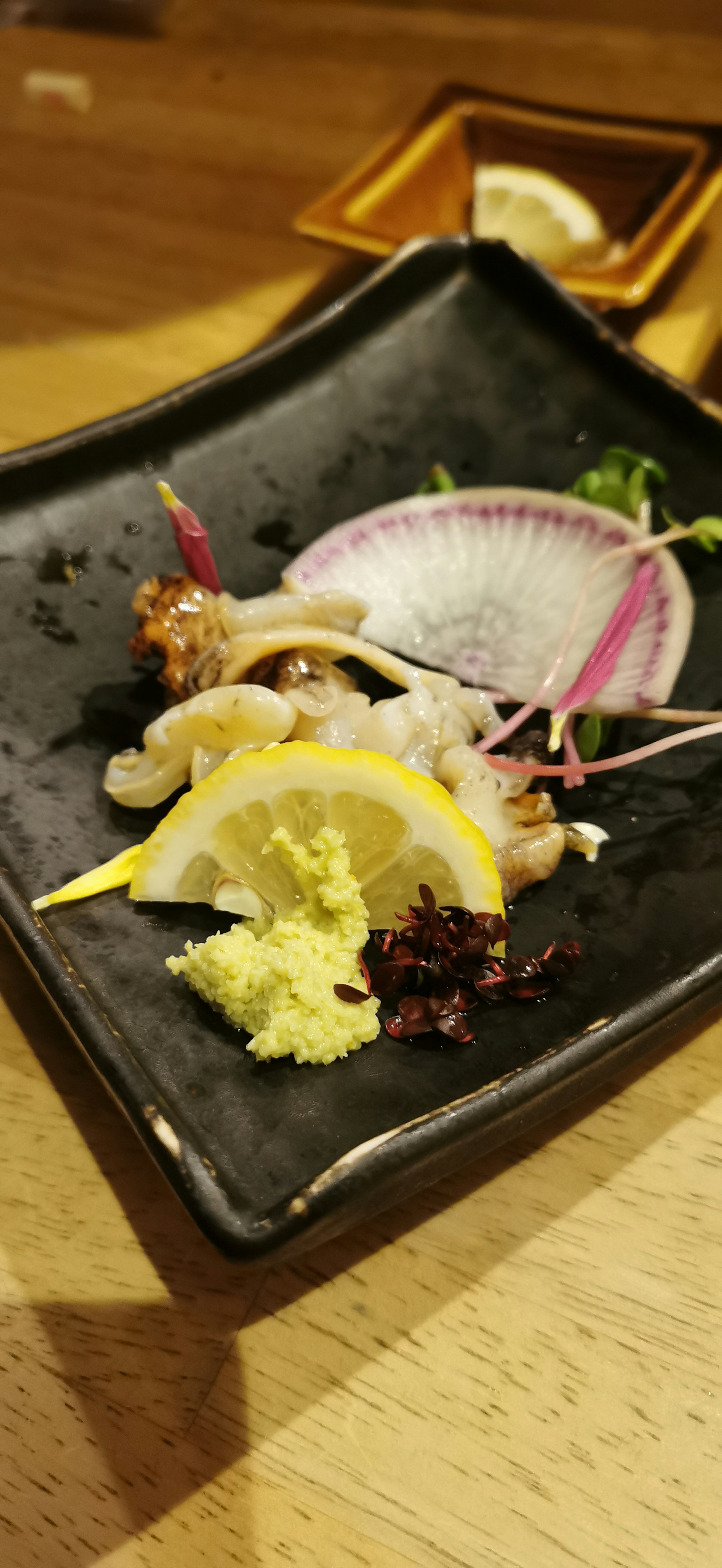 Fresh sashimi served on a black plate with lemon slices