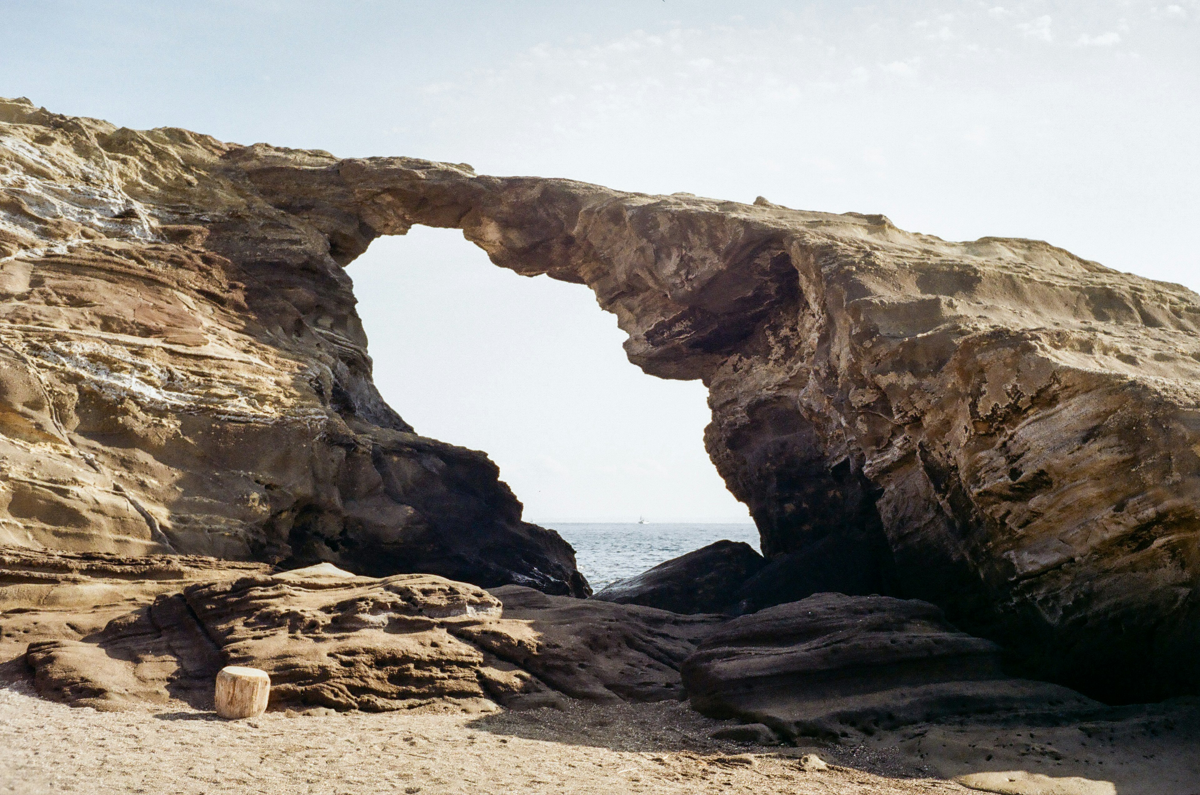 Ein großer Felsbogen, der auf das Meer zeigt, mit einem Sandstrand