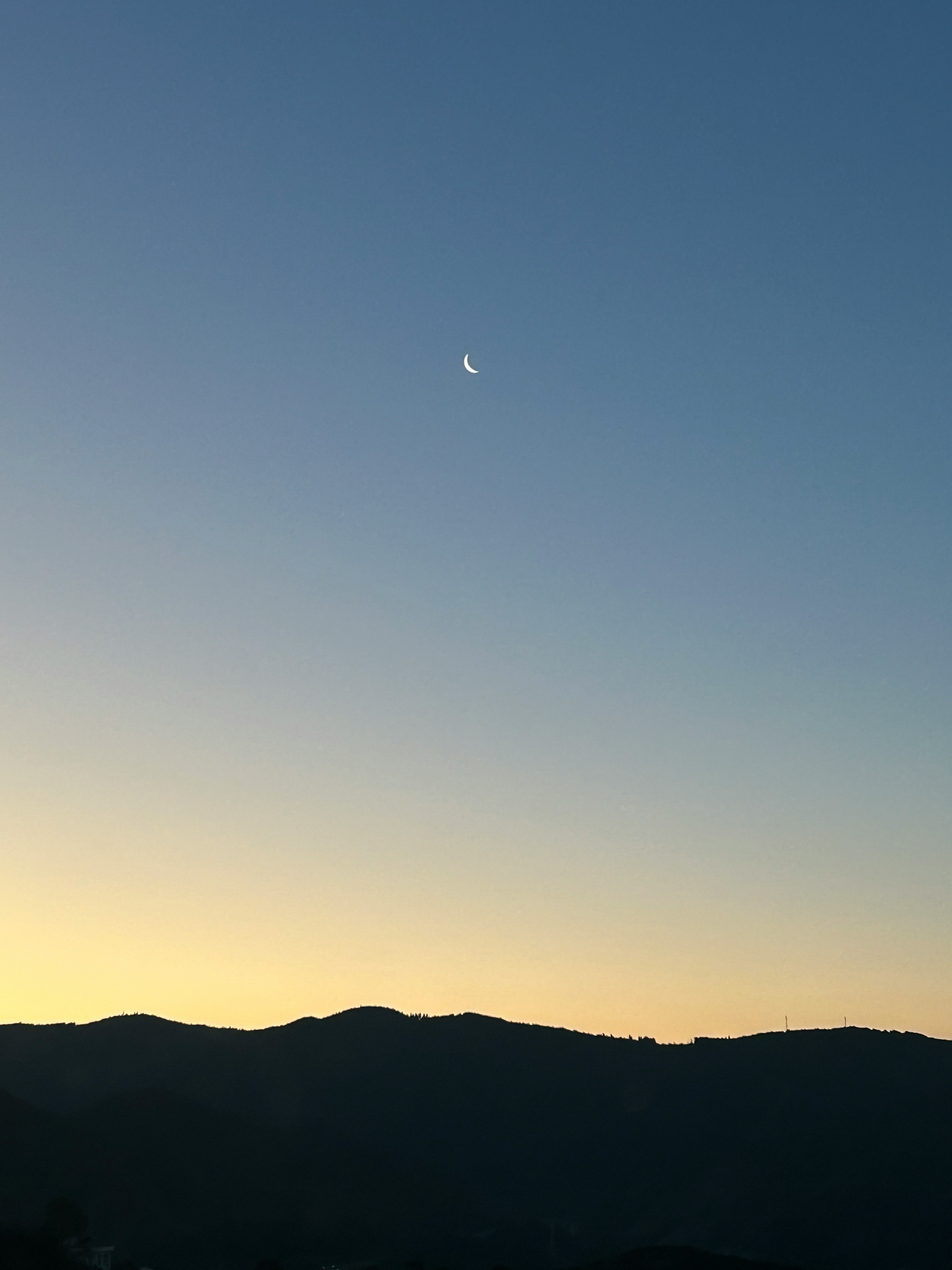 Luna creciente en un cielo brillante con silueta de montañas