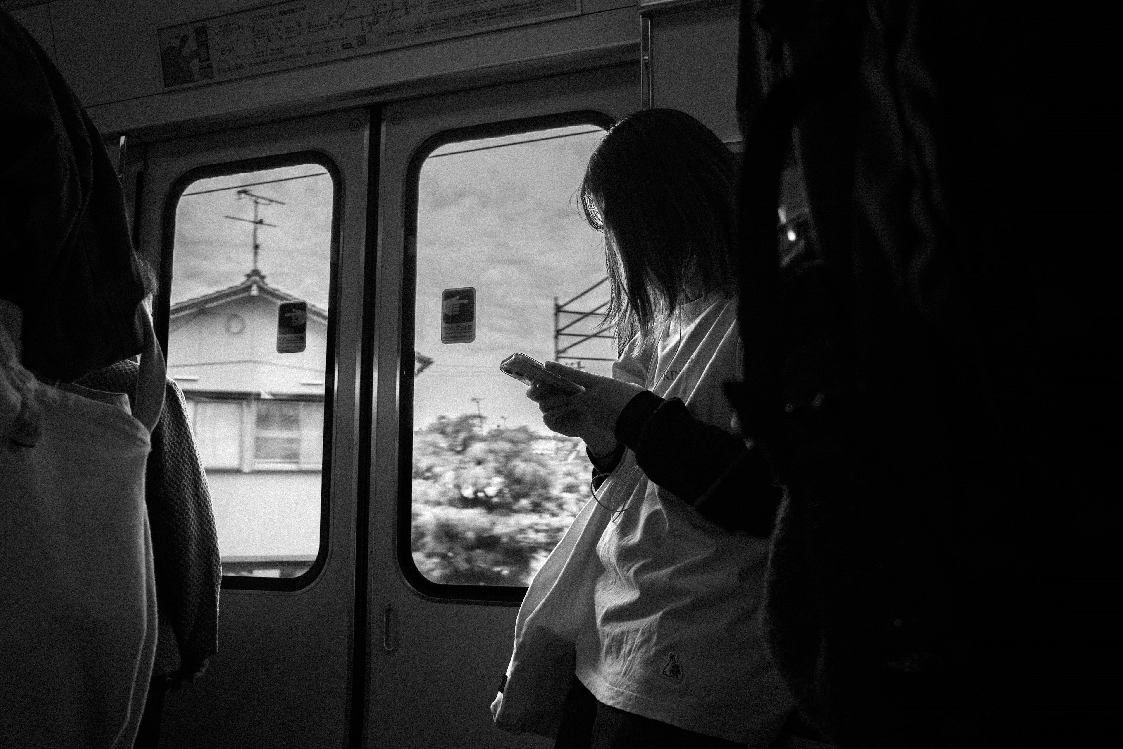 Une femme tenant un smartphone dans un train en noir et blanc avec une vue sur une maison à l'extérieur