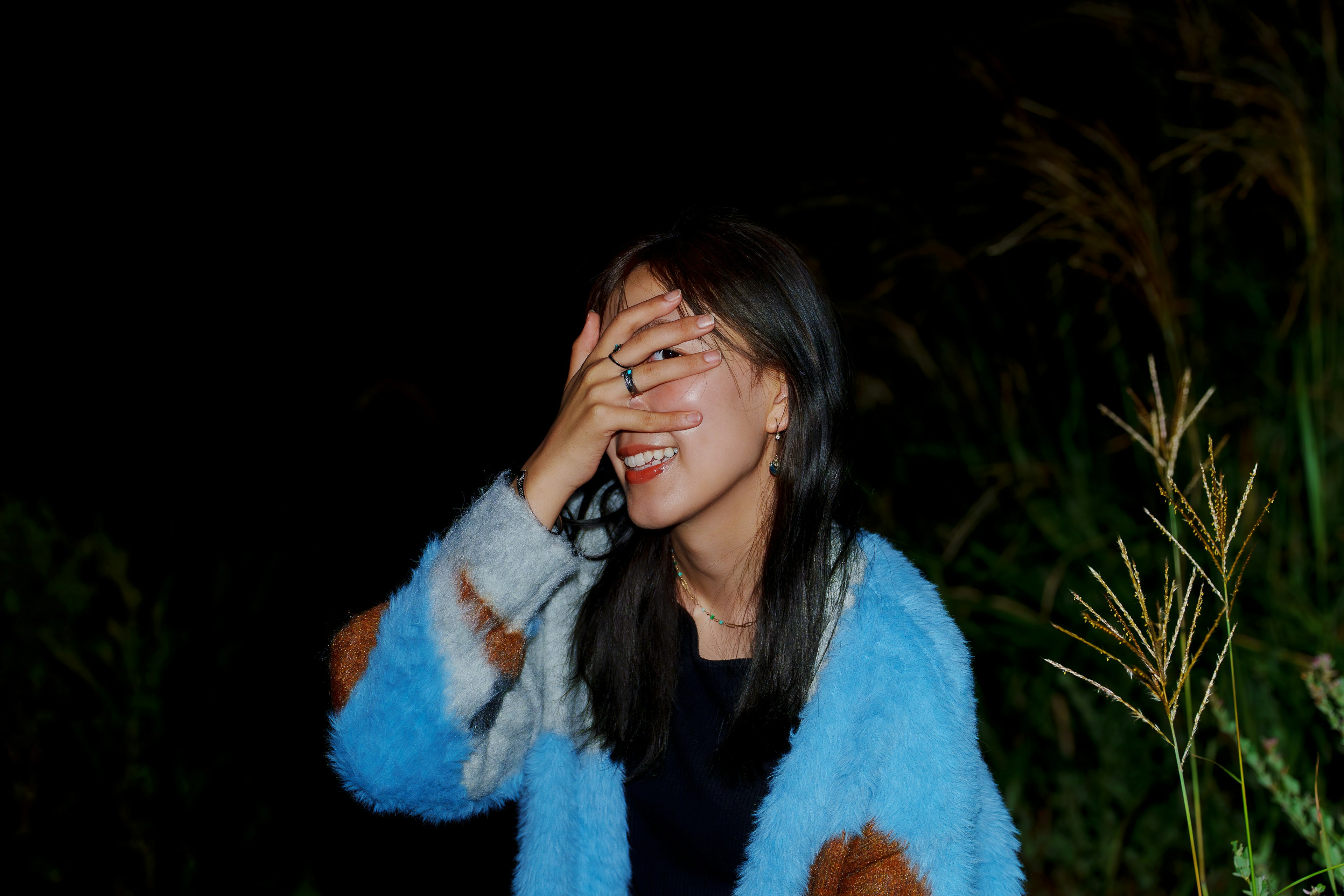 A smiling woman covering her face with her hand in a dark setting