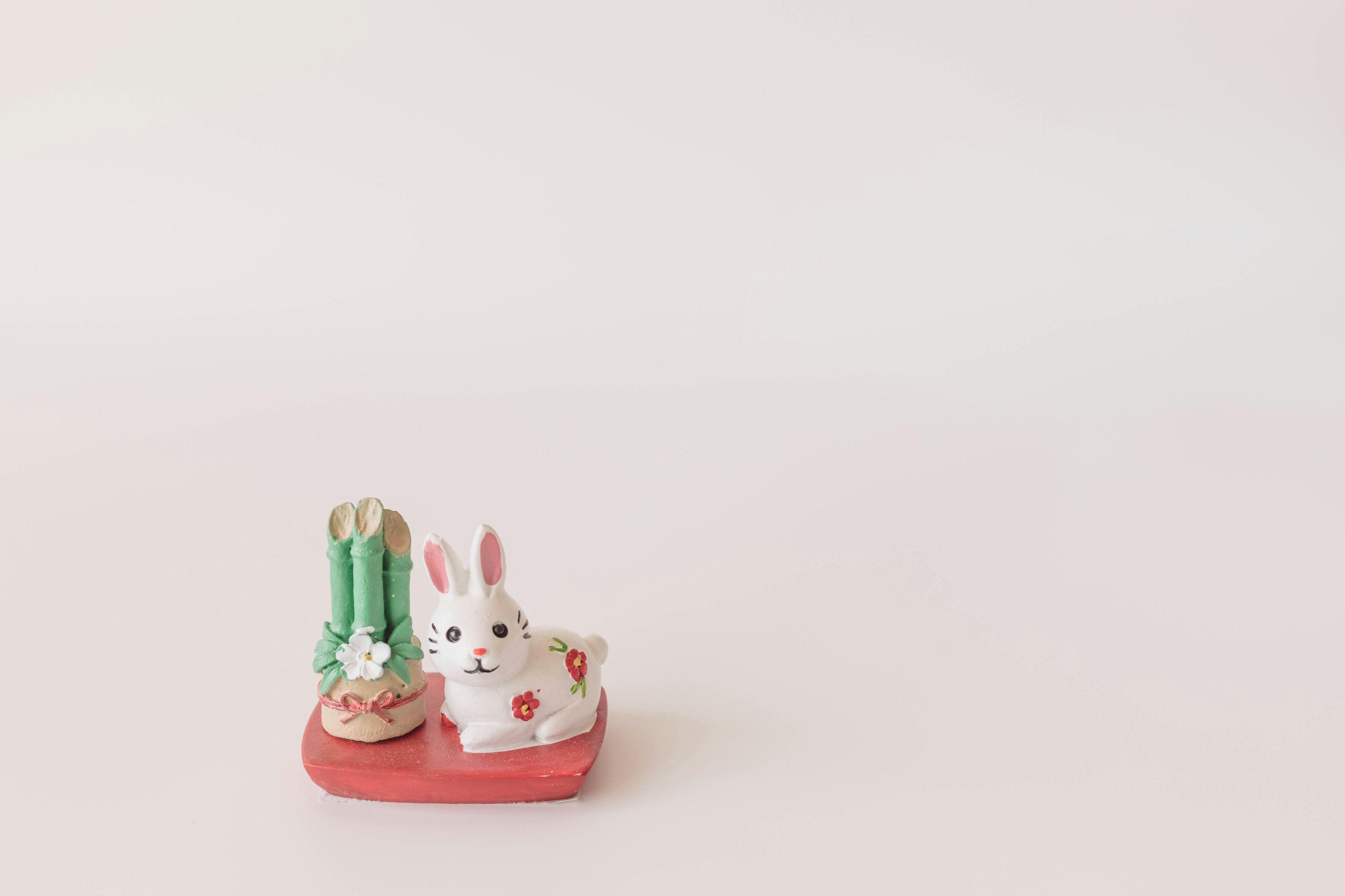 Figurine de lapin blanc sur une base rouge avec une décoration en bambou vert sur un fond blanc