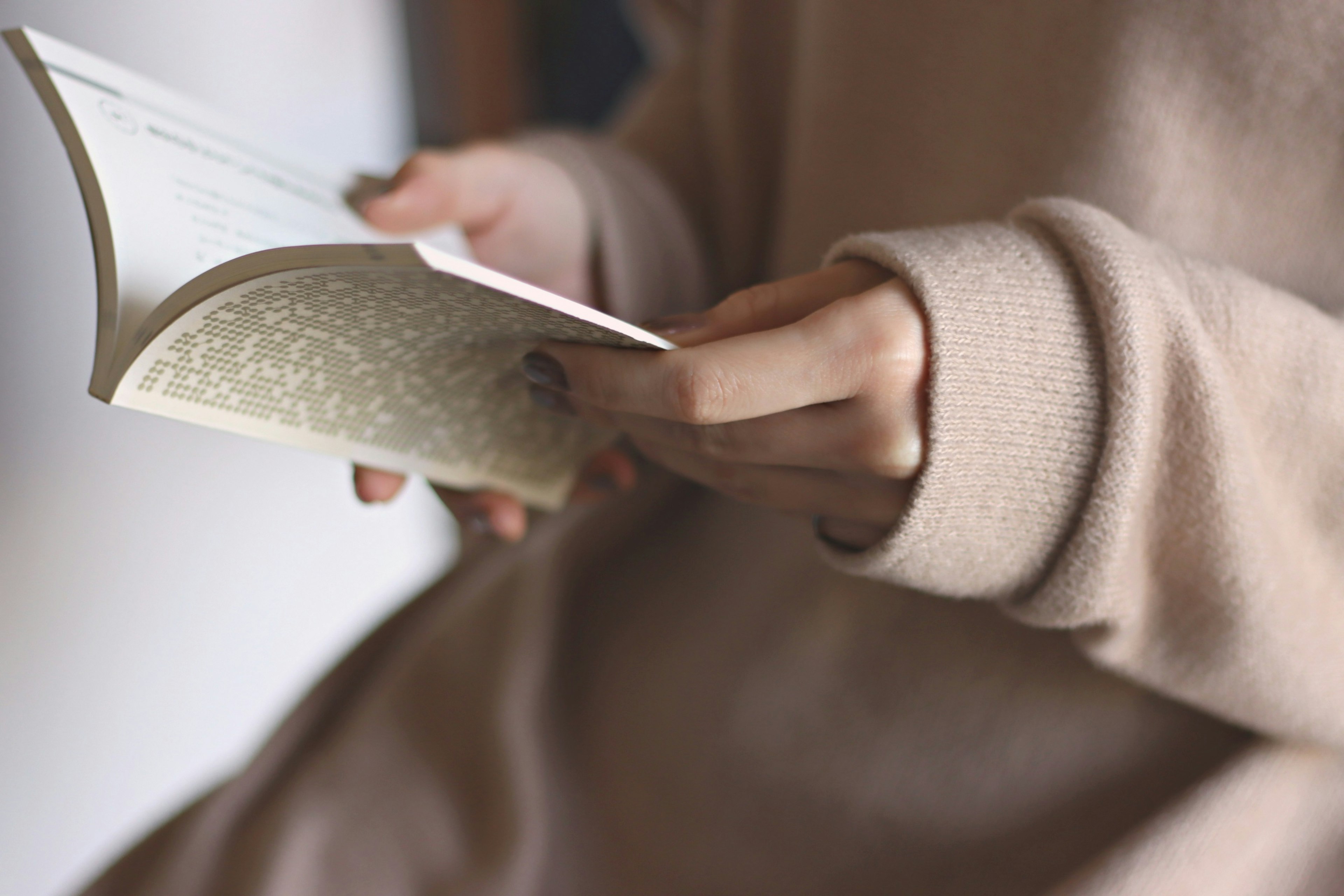 A person holding a book wearing a soft beige sweater