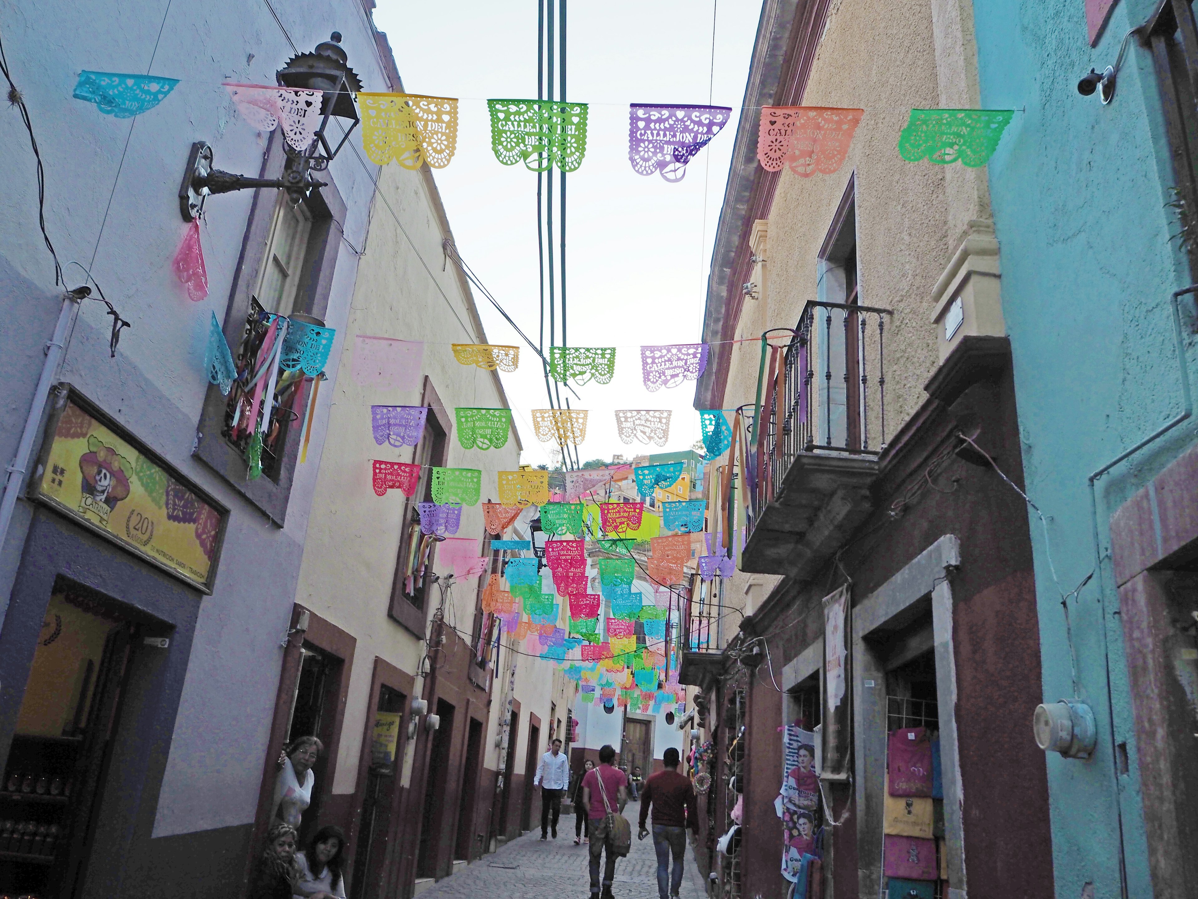 Colorful papel picado decorations hanging above a lively street with people walking