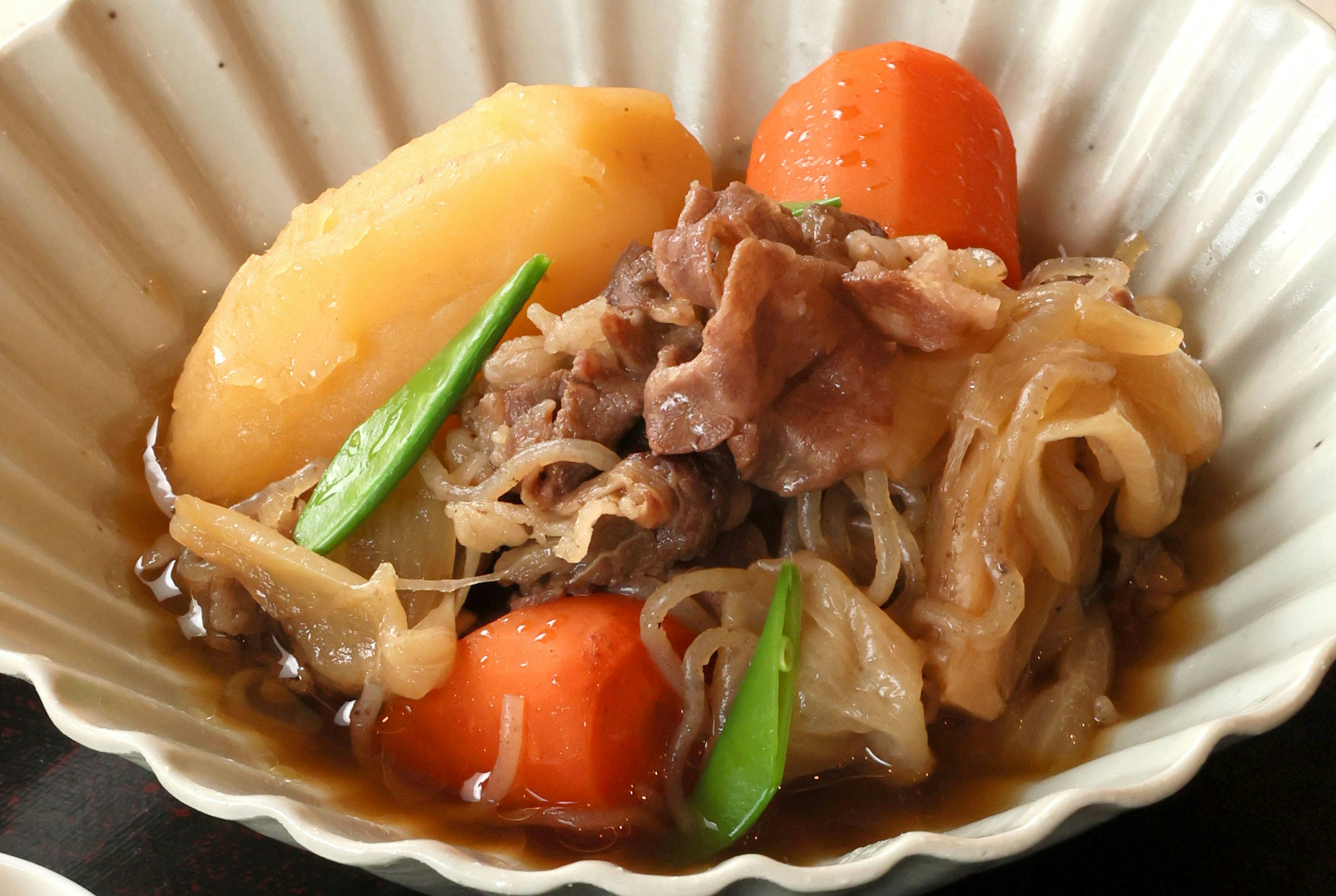 Nikujaga giapponese con patate, carote, manzo e shirataki servito in un piatto scallopato