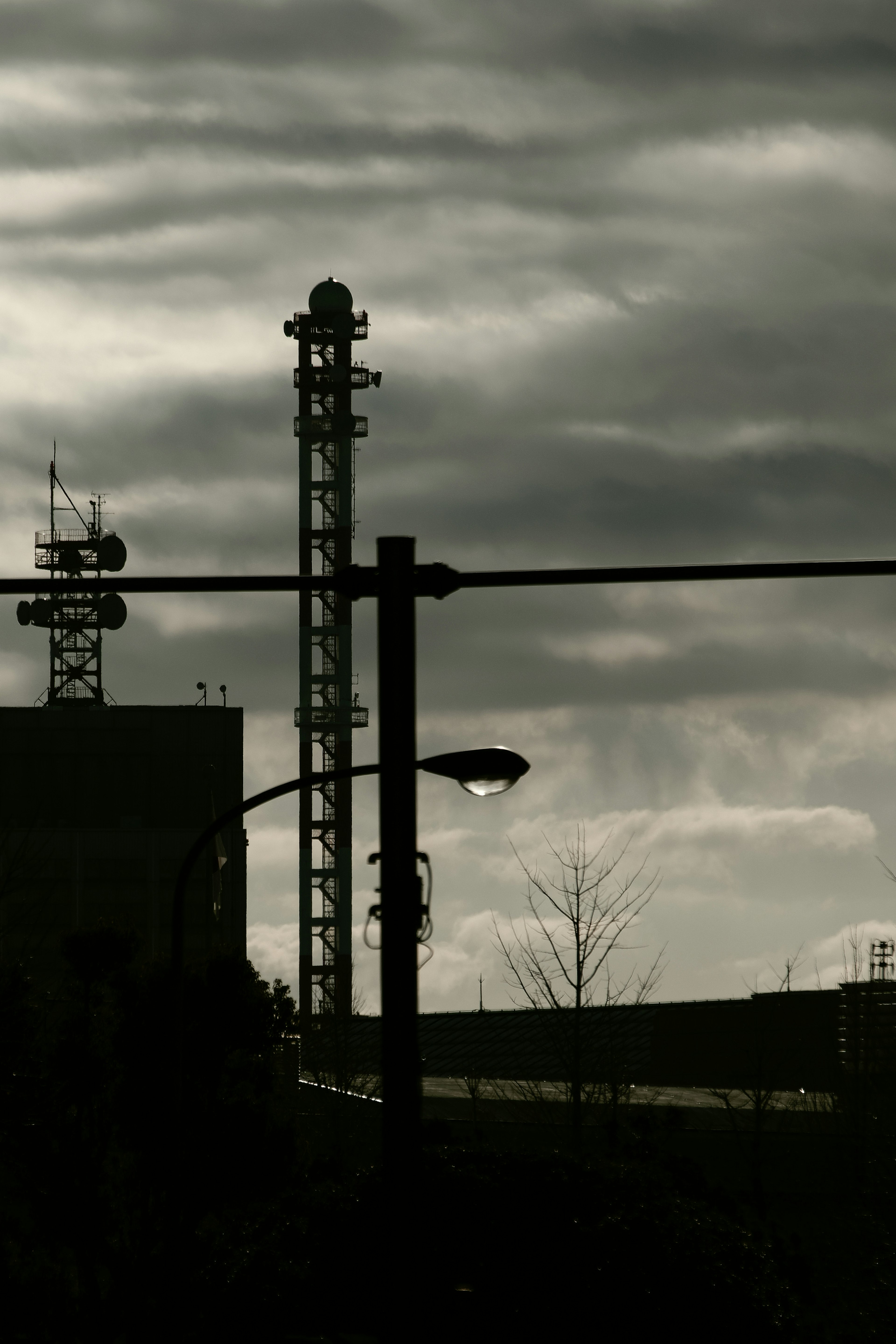 Silhouette eines hohen Turms und einer Straßenlaterne unter dunklen Wolken