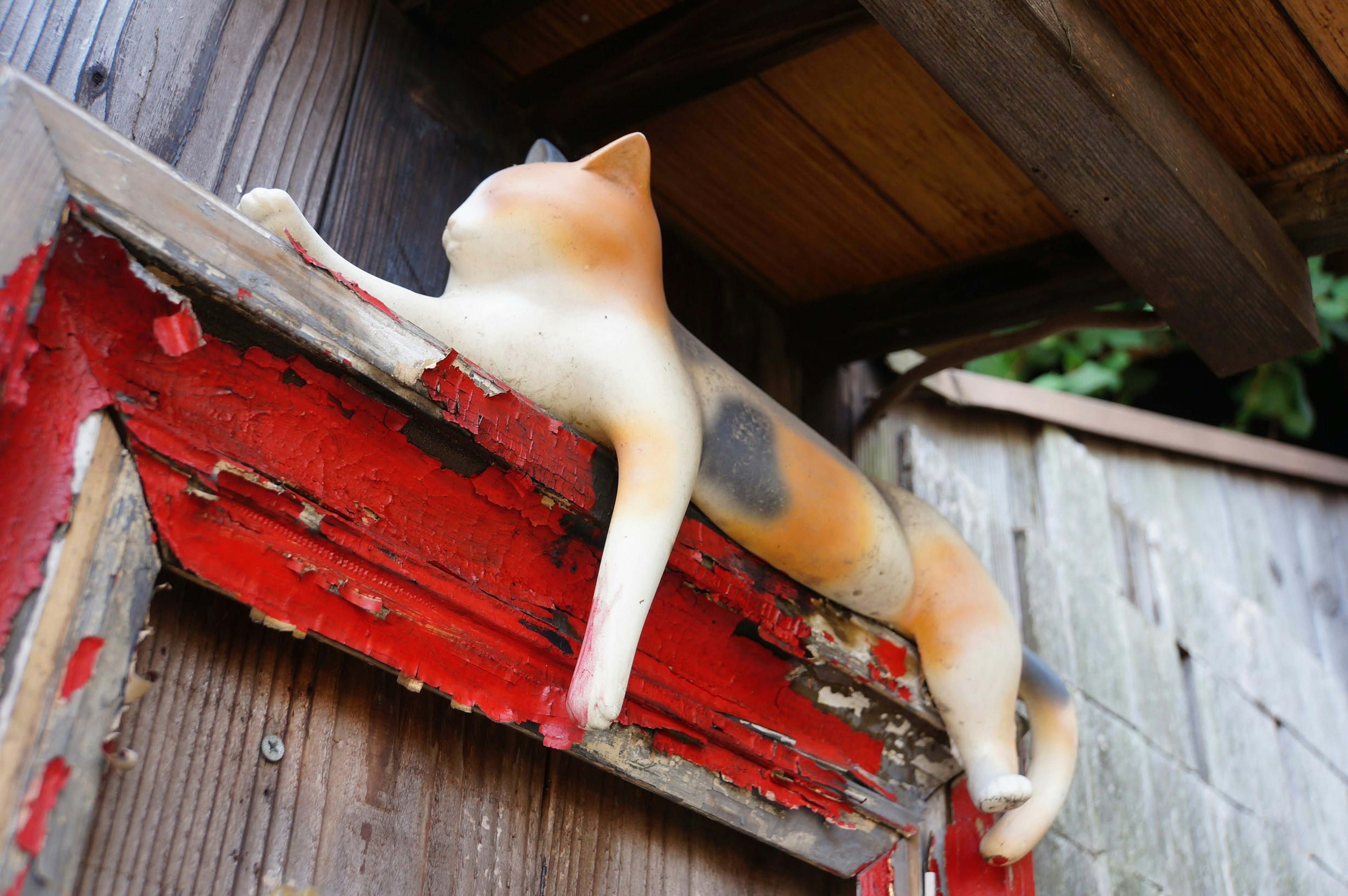 Una escultura de gato descansando sobre una viga de madera roja