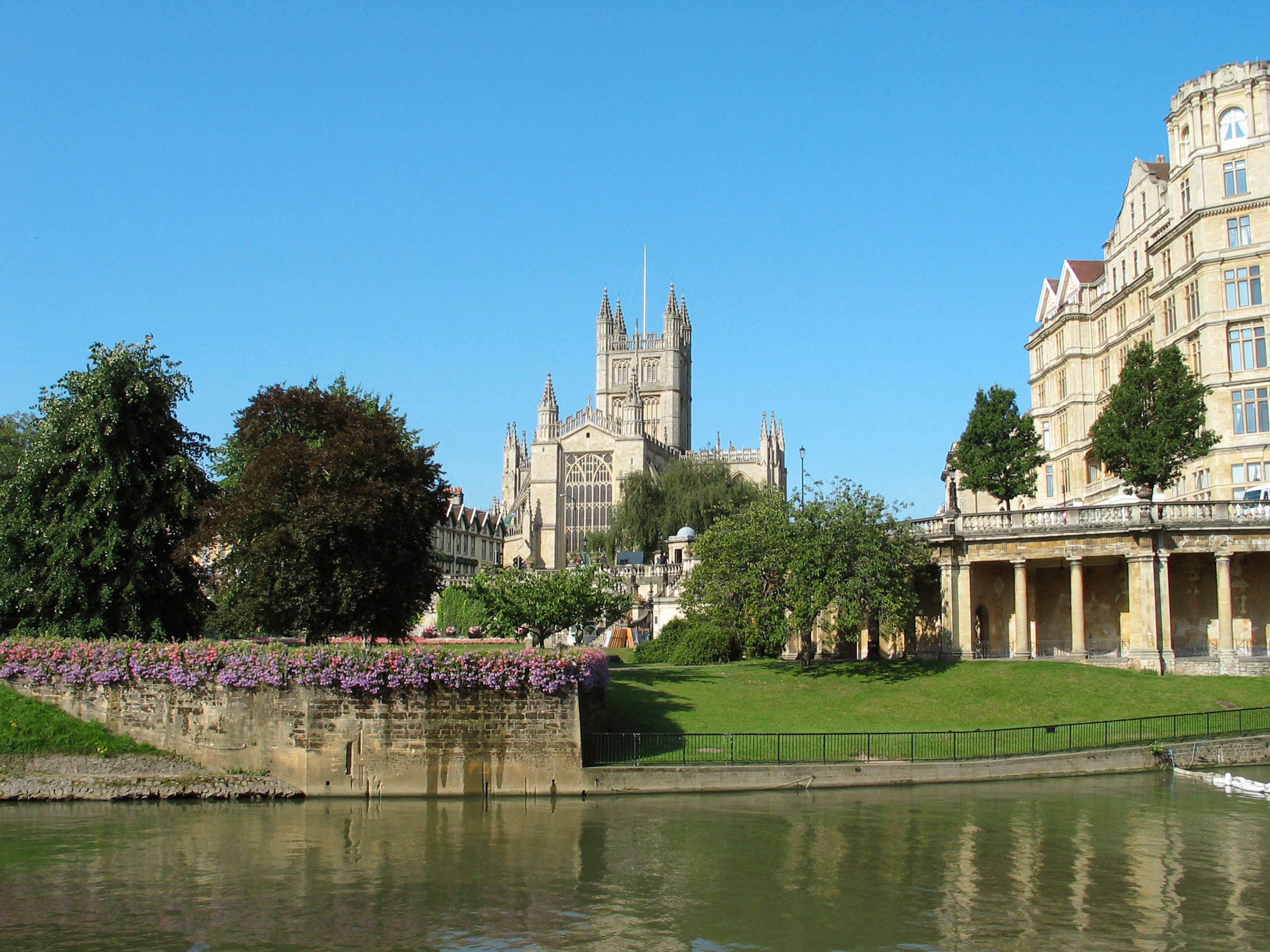 Historic building and lush greenery by the river under a clear blue sky