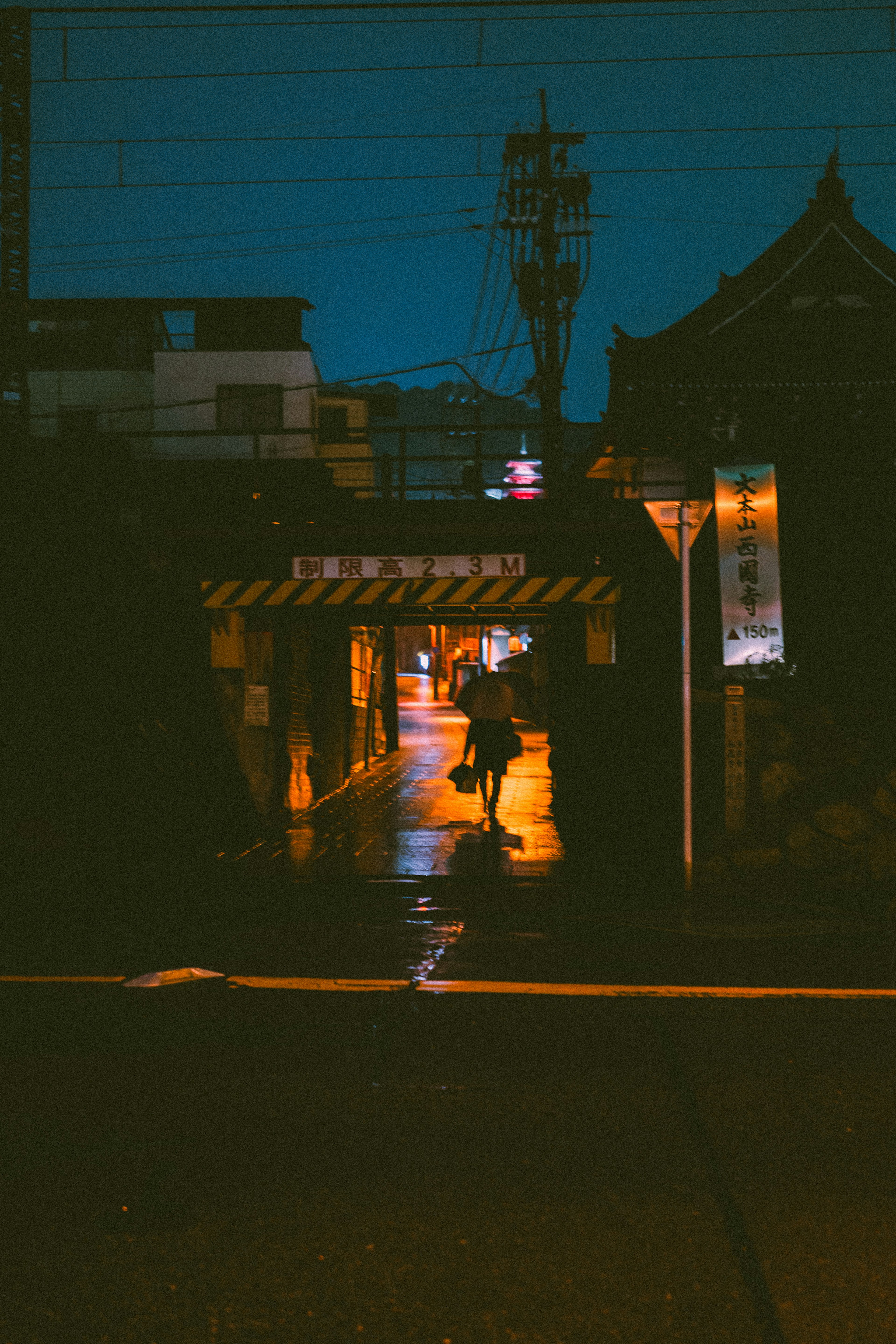 Une personne marchant dans une ruelle mouillée par la pluie la nuit, éclairée par des lampadaires orange