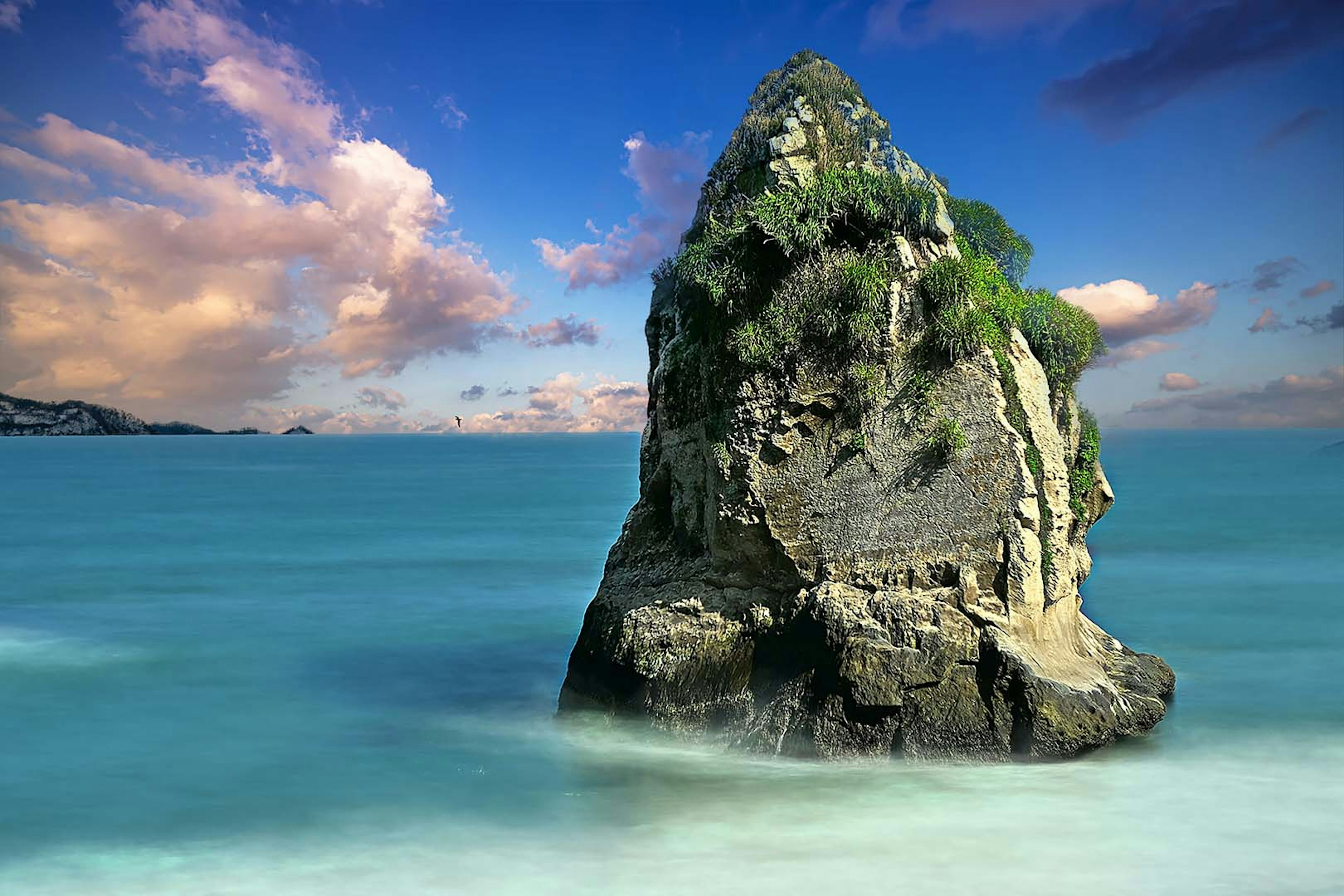 青い海と空の下に立つ大きな岩と雲