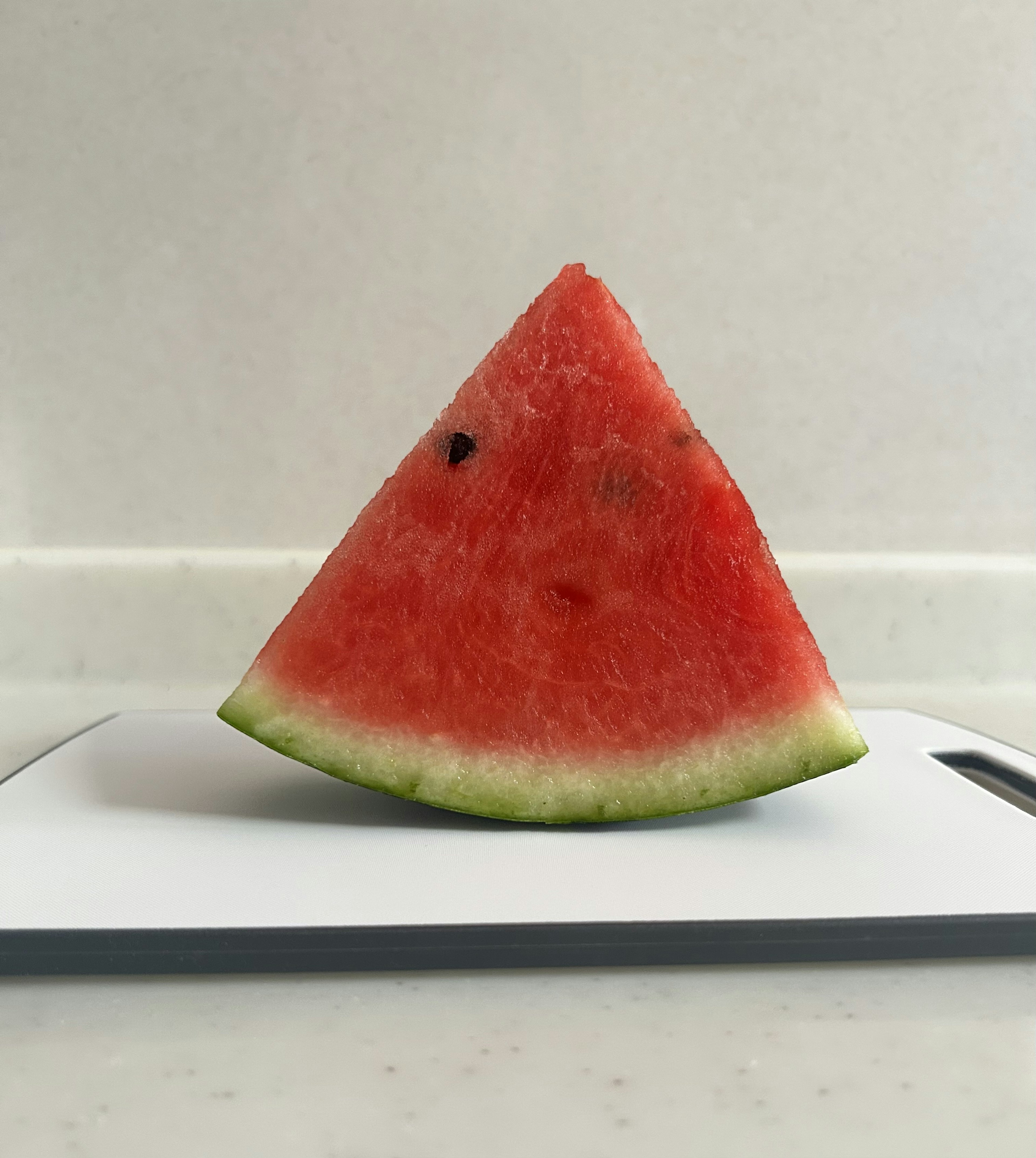 Ein dreieckiges Stück Wassermelone auf einem weißen Schneidebrett