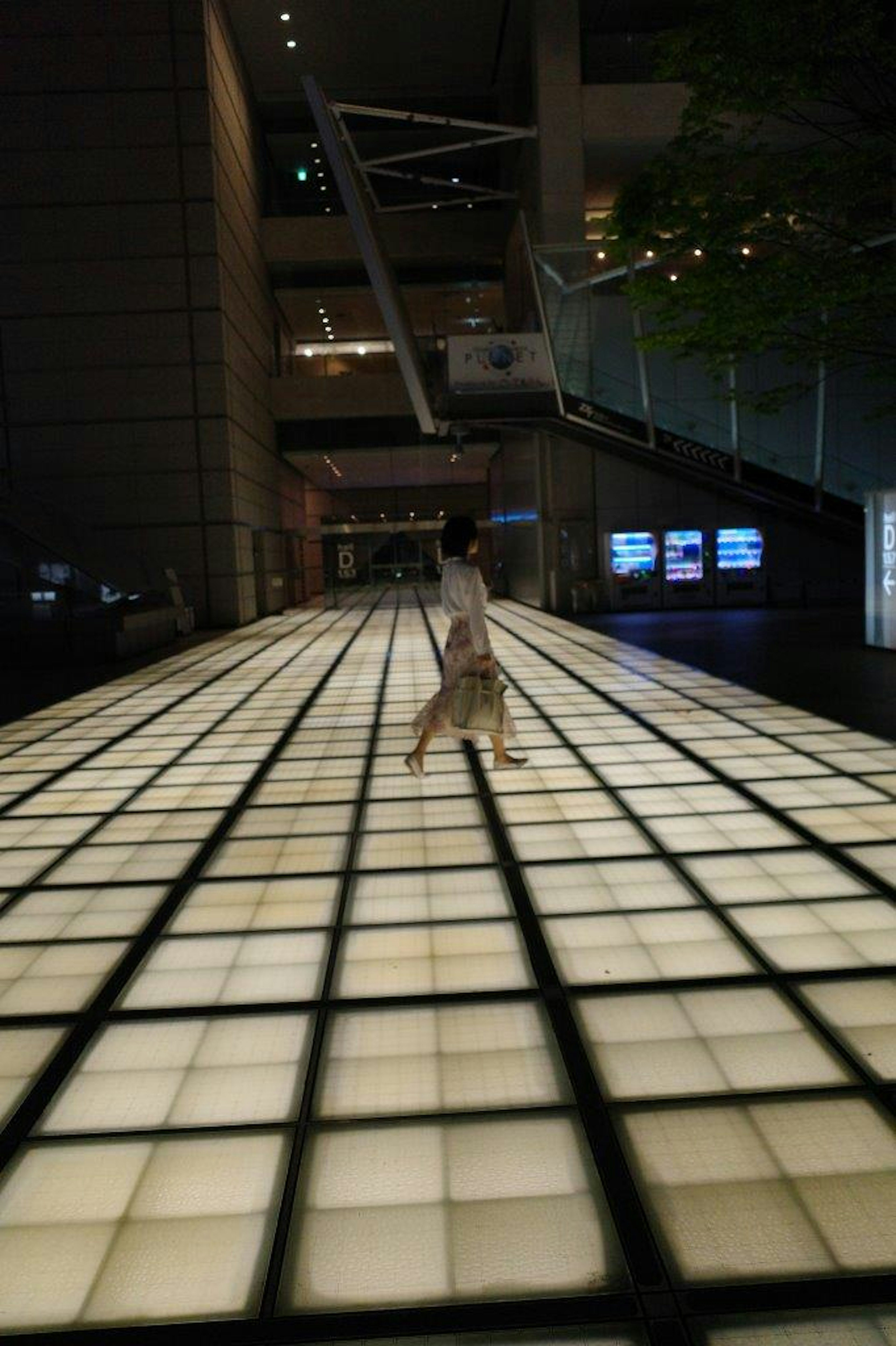 Person walking on a glowing tiled floor in a modern building interior with bright lighting