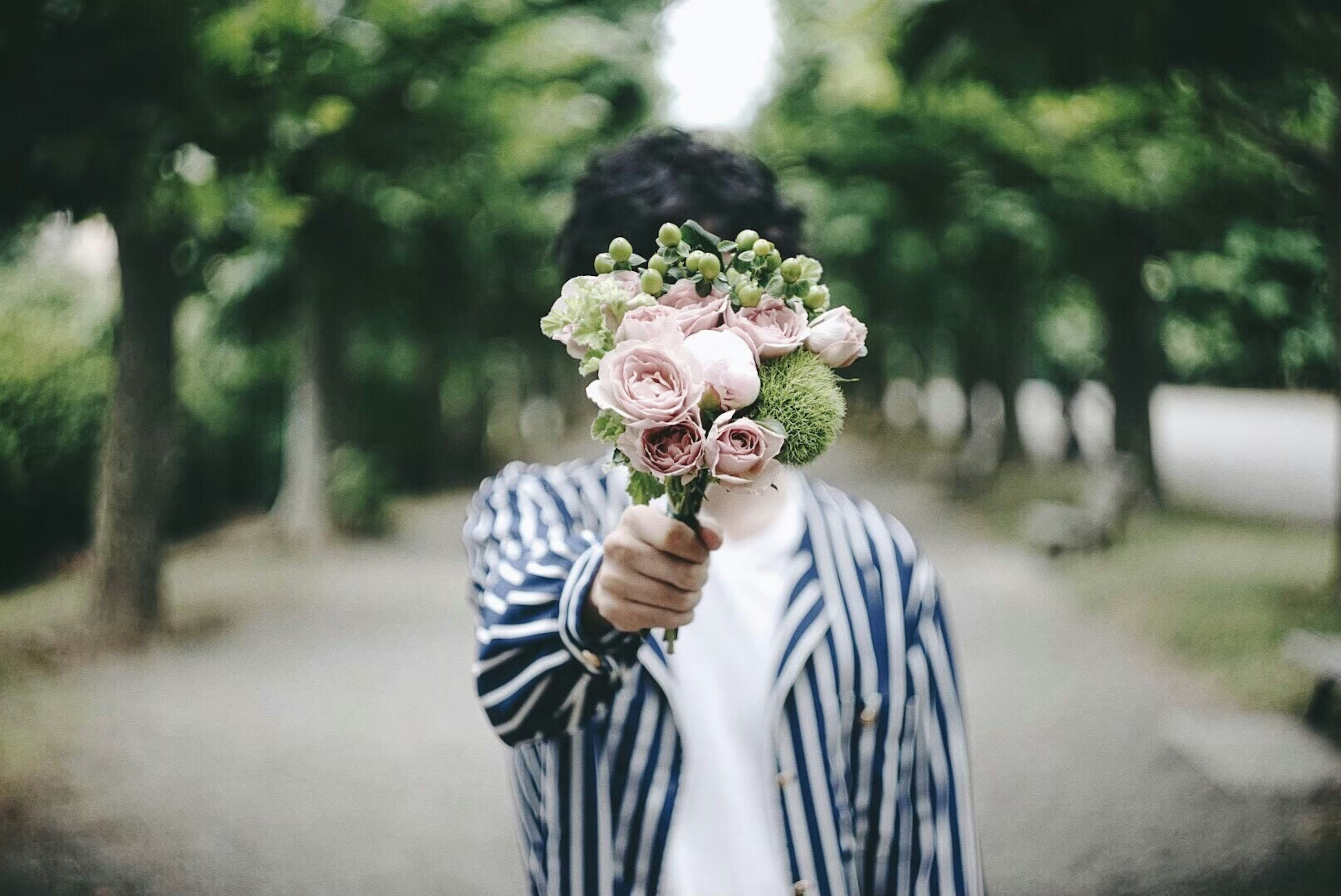 Persona con chaqueta a rayas sosteniendo un ramo de flores en un parque