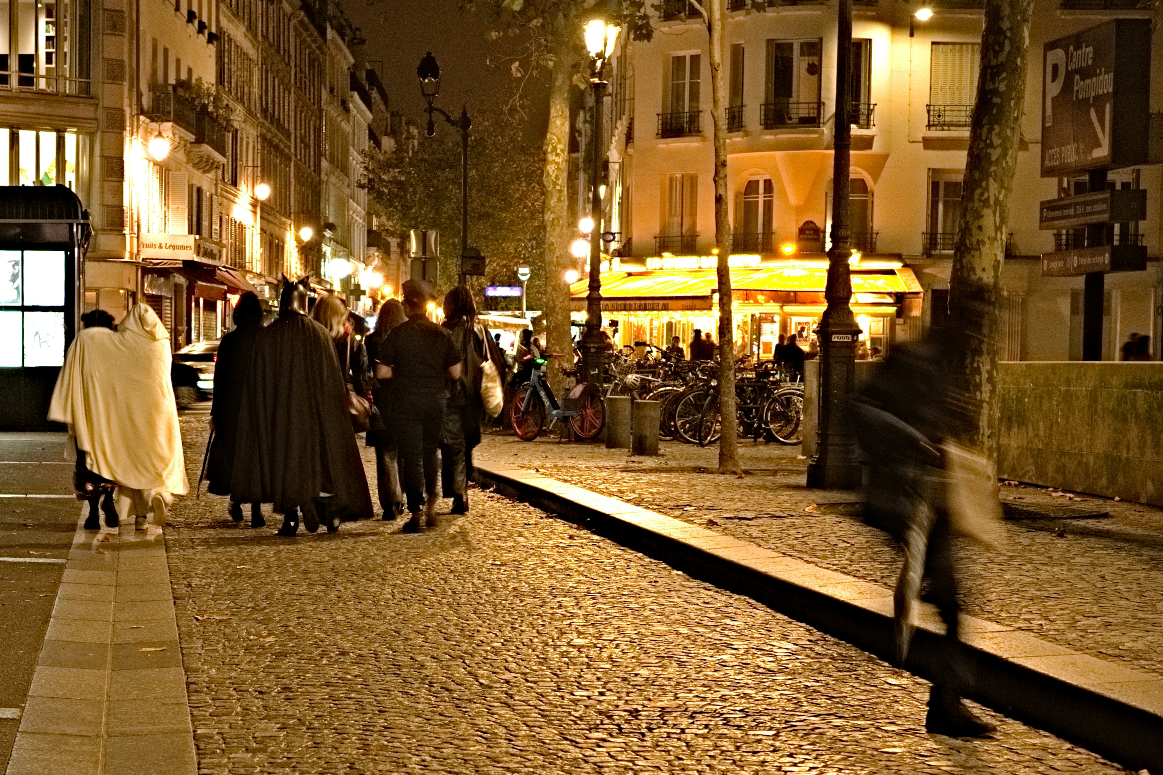 Menschen, die nachts auf einer Kopfsteinpflasterstraße in Paris mit einem beleuchteten Café gehen