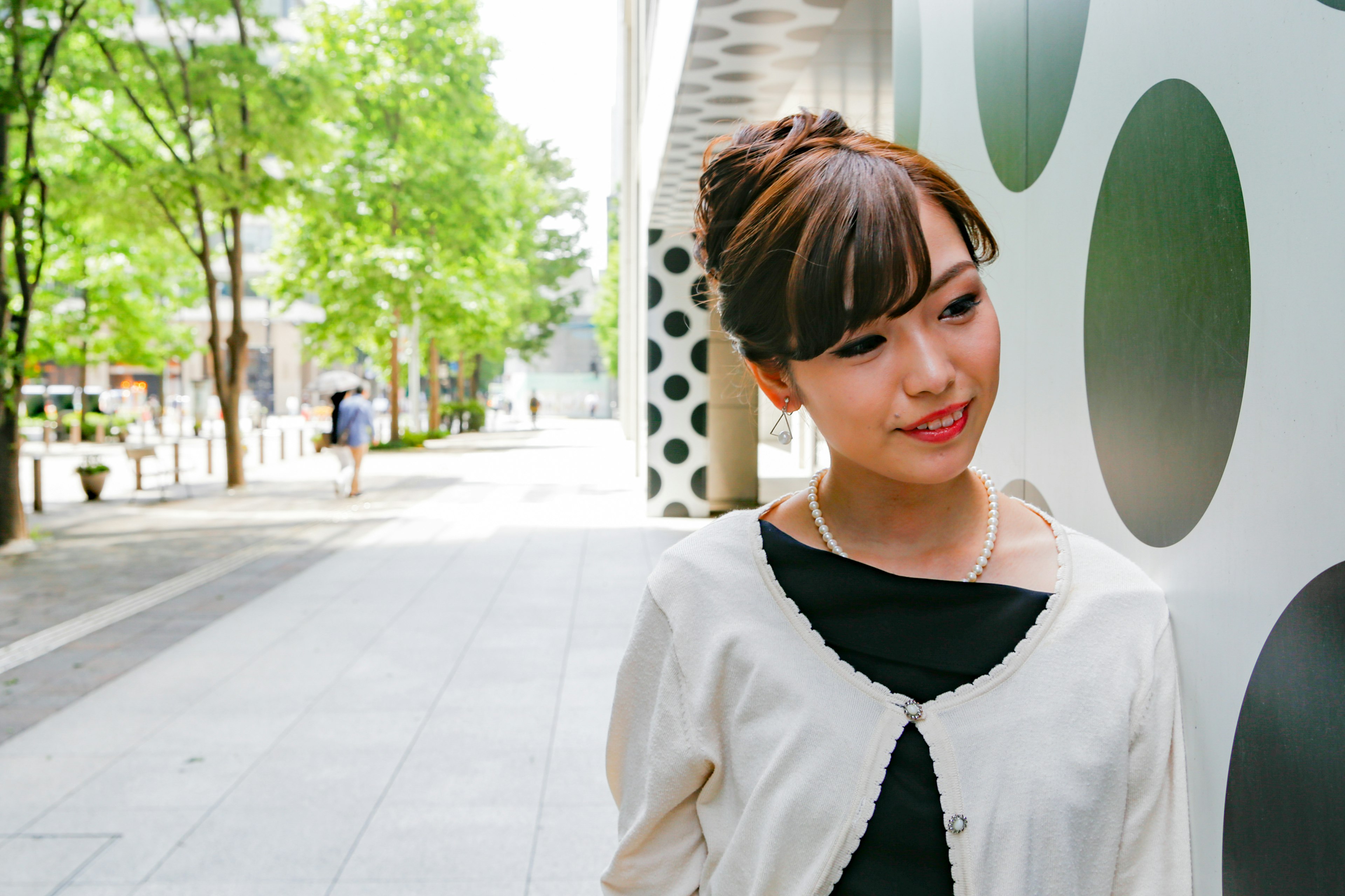 A woman smiling on the street with green trees and a modern building backdrop