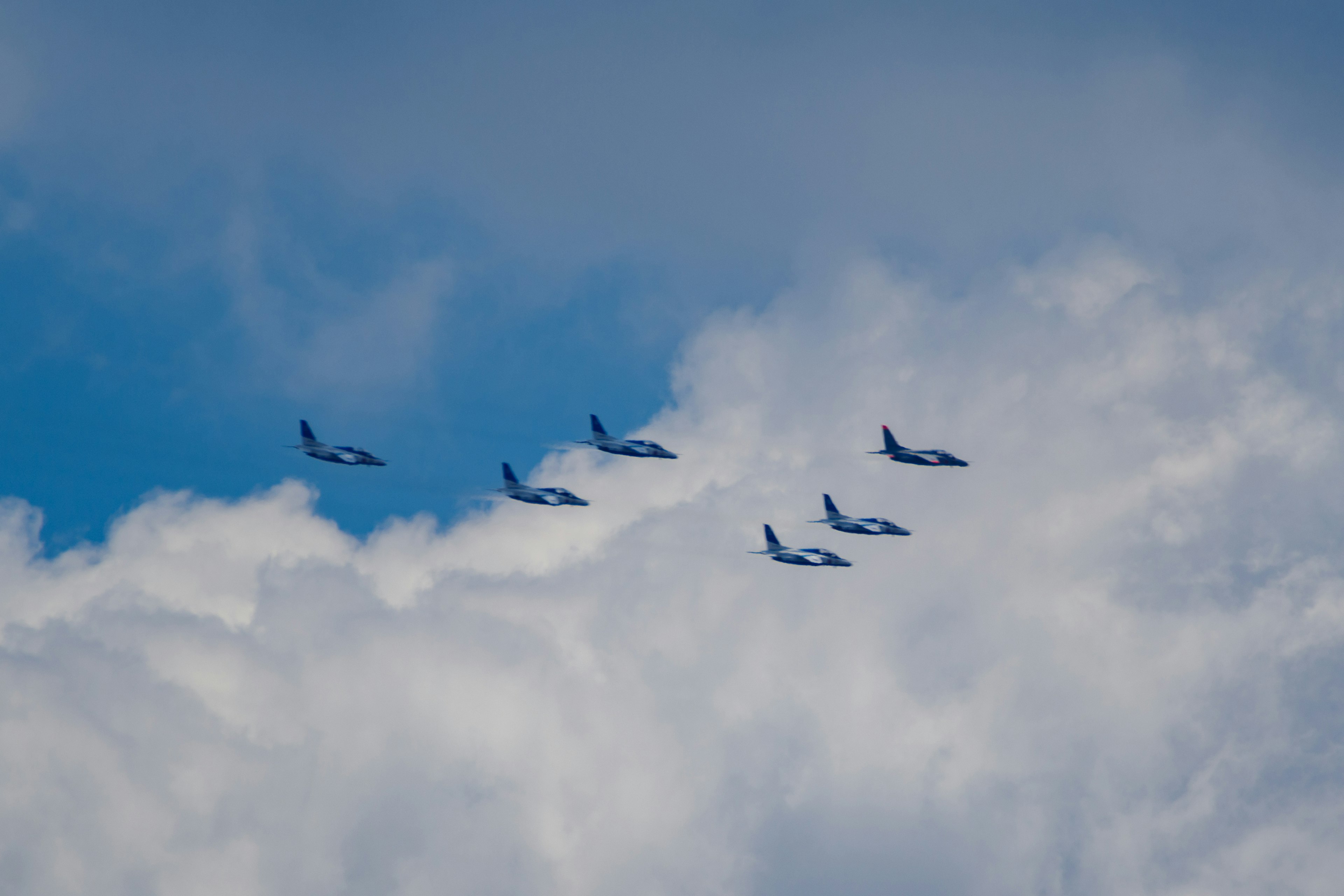 A formation of several aircraft flying through white clouds in a blue sky