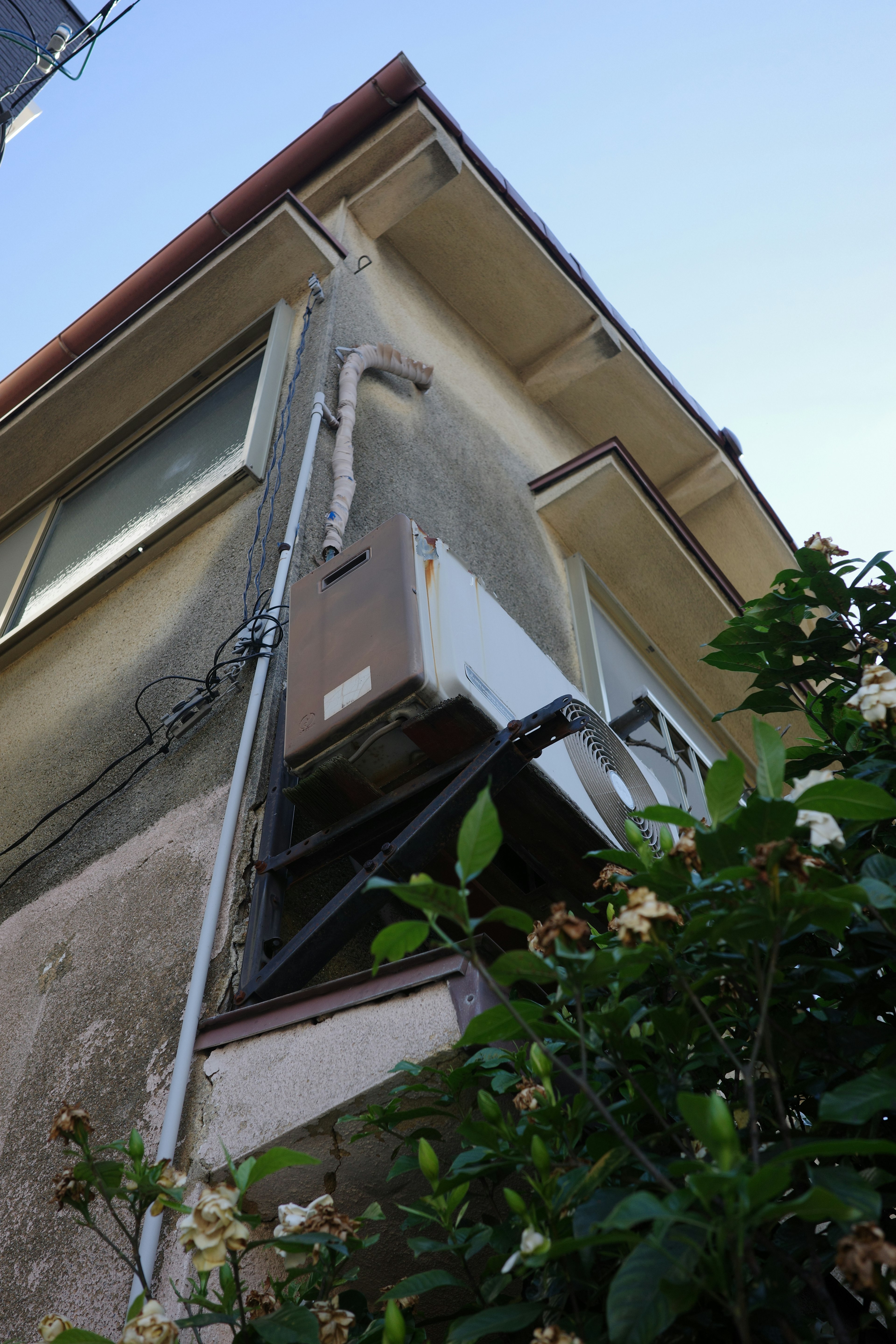 Vue latérale d'un vieux bâtiment avec un climatiseur et un feuillage vert