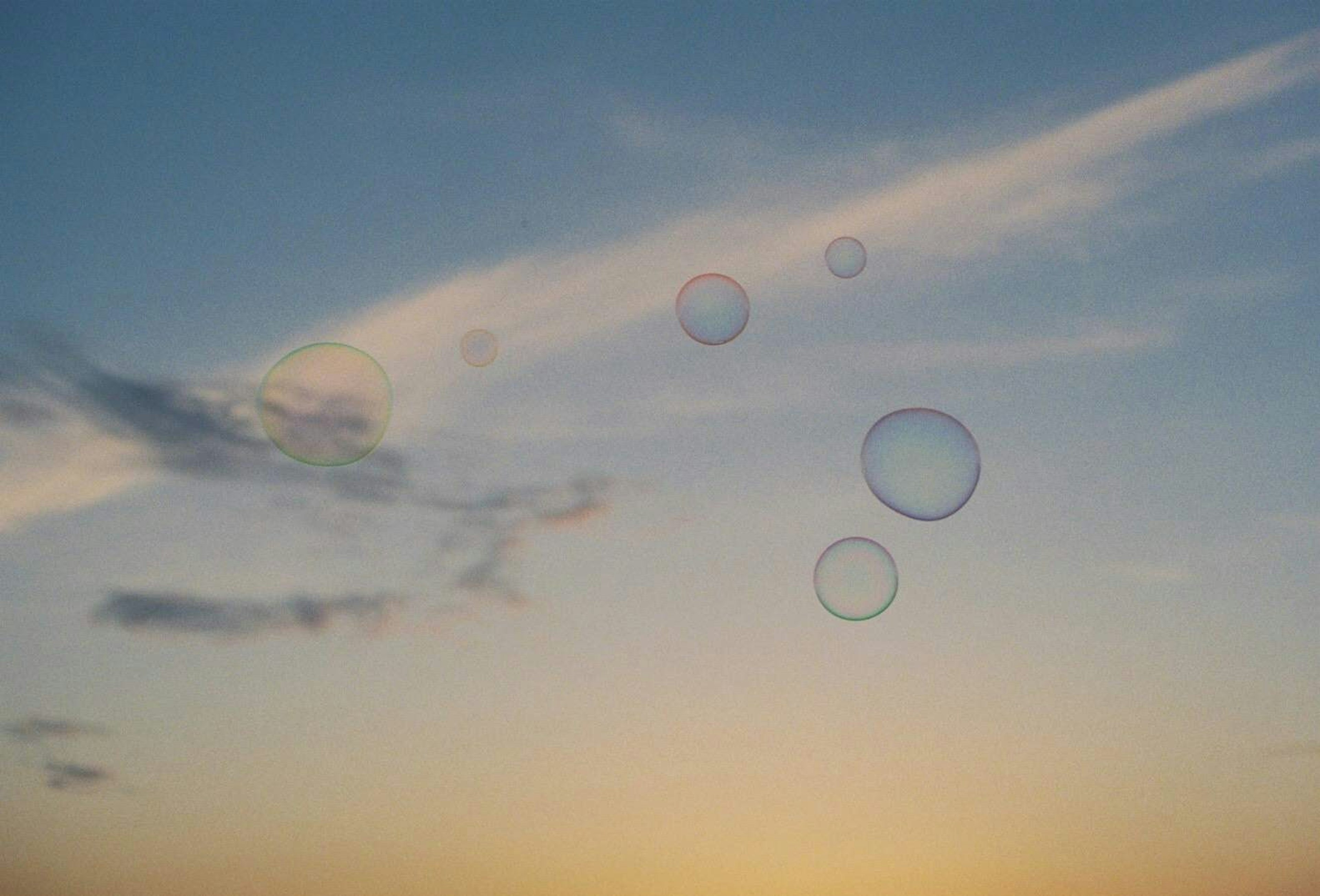 Bubbles floating in a blue sky with soft clouds at sunset