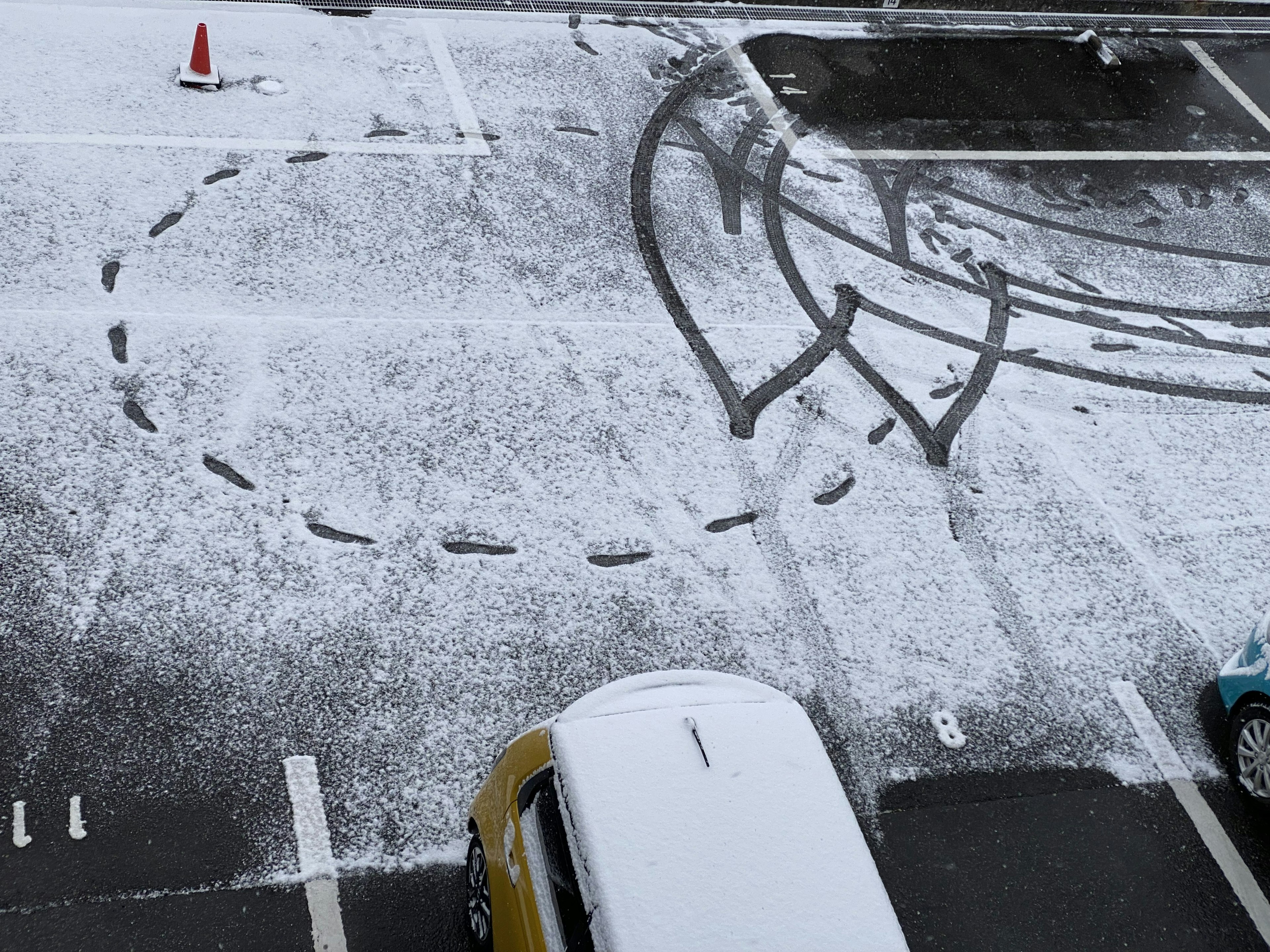 Snow-covered parking lot with circular tire tracks and a cone