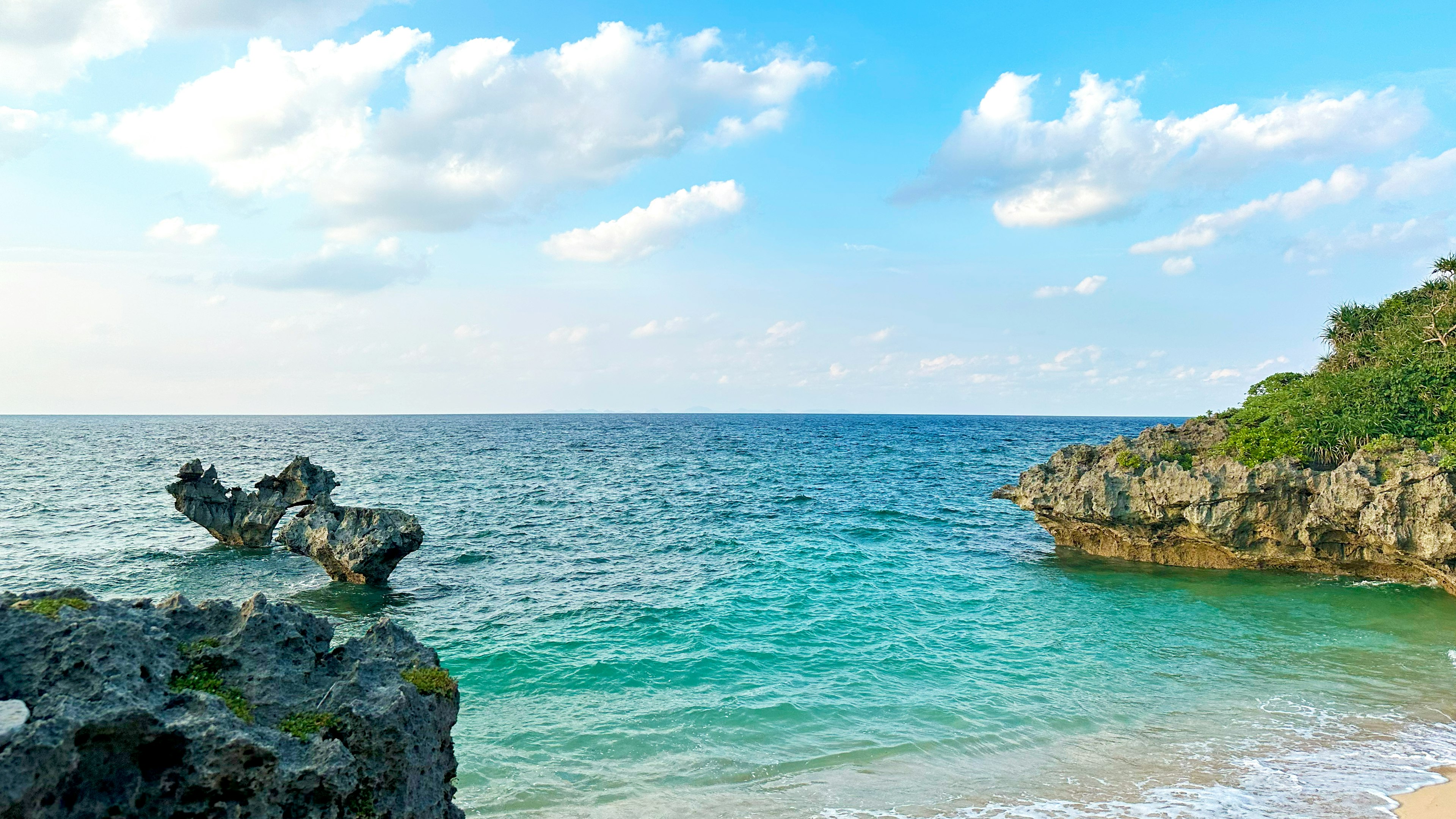 Beautiful view of blue sea and sky featuring rocky formations and white sandy beach