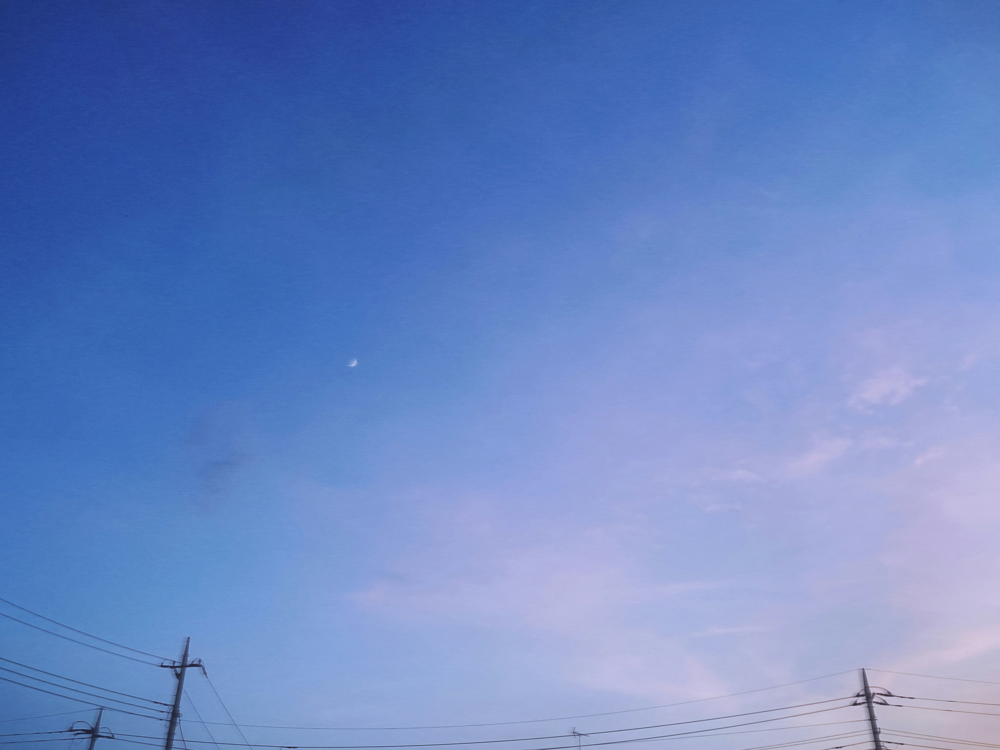 Langit biru cerah dengan awan lembut dan bulan yang terlihat