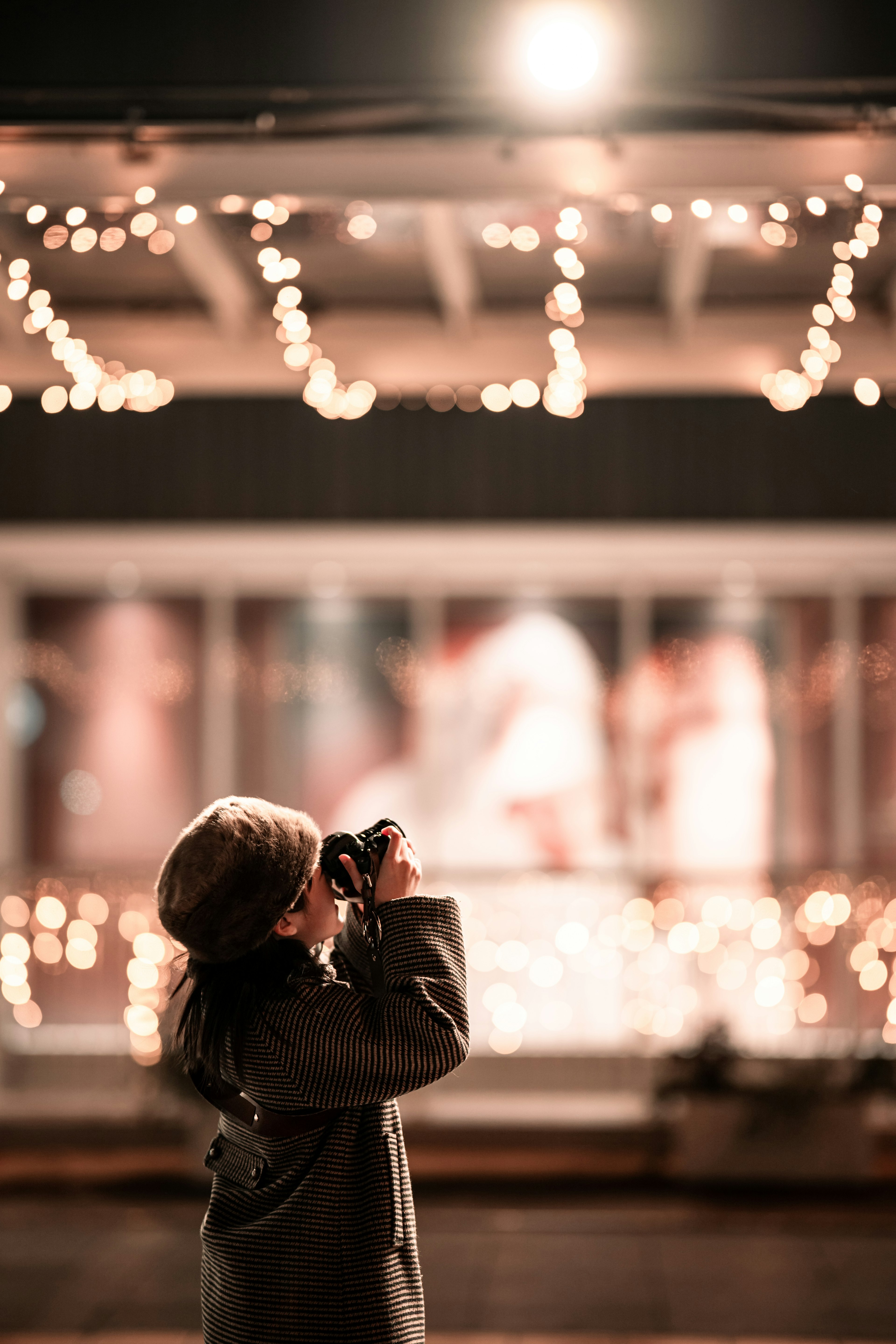 Une fille prenant des photos avec un appareil photo dans une rue nocturne décorée de lumières féeriques