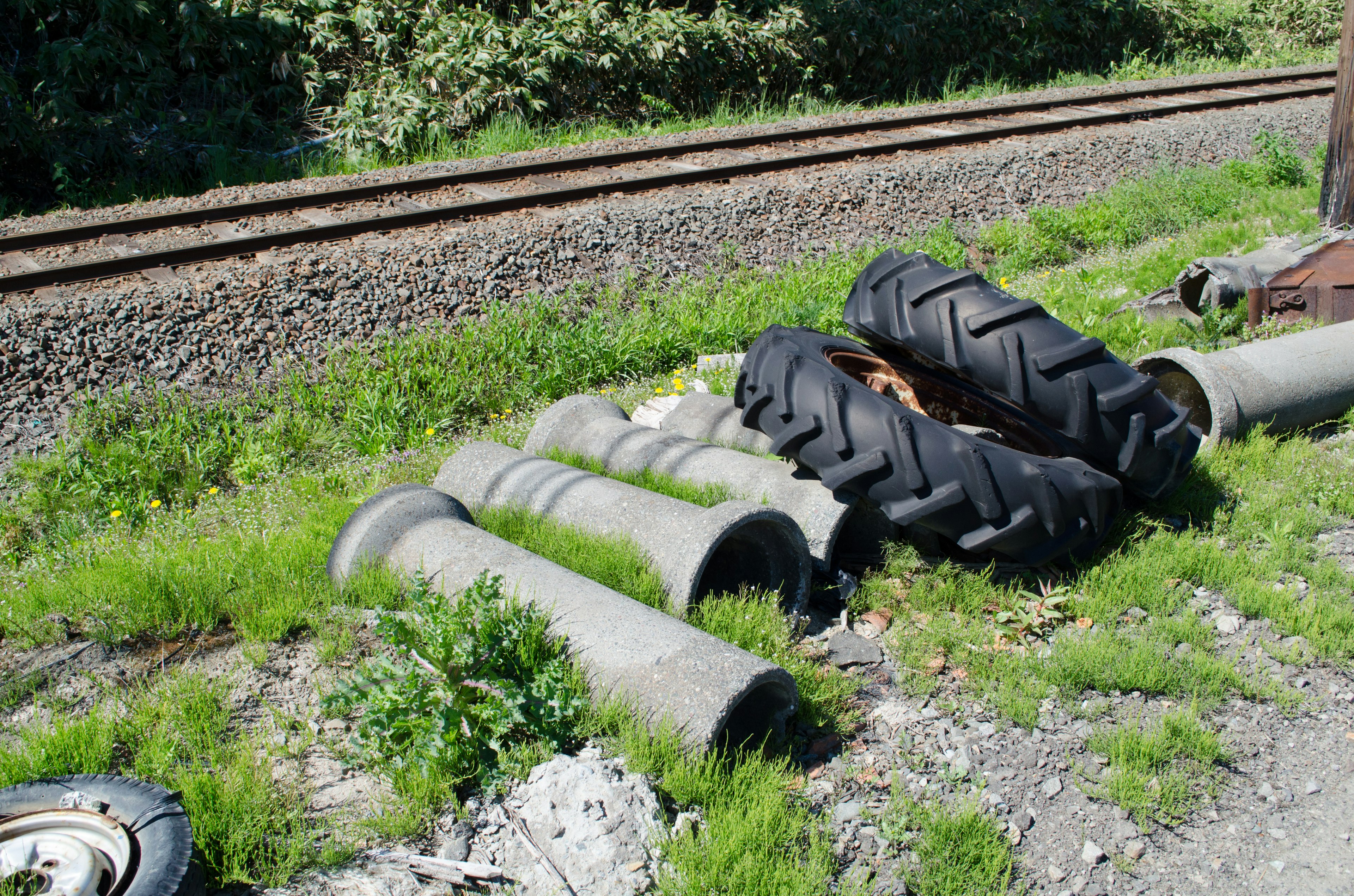 Concrete pillars and tractor tires resting on grass near the railroad