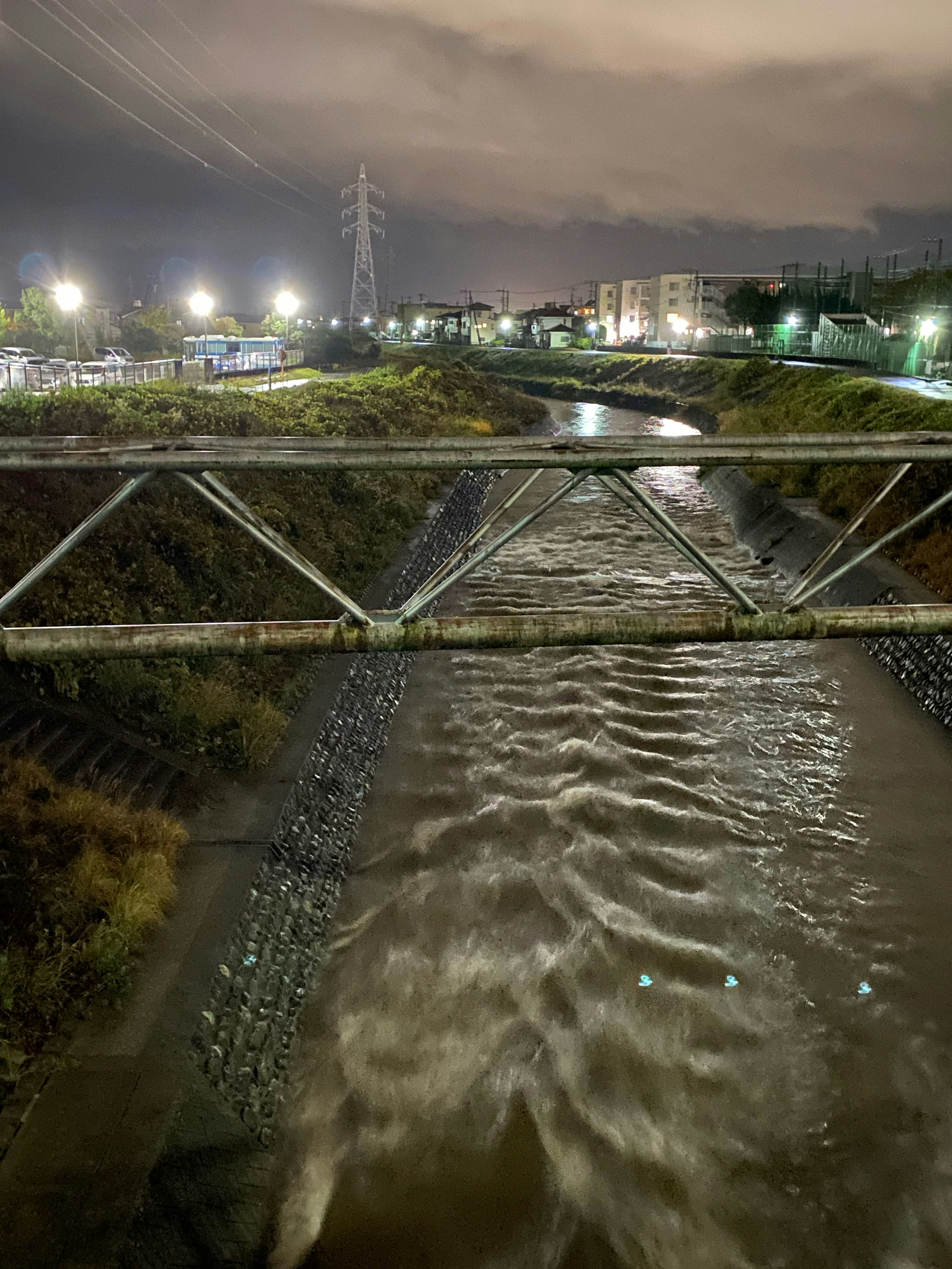 Jembatan logam di atas sungai di malam hari dengan lampu jalan di sekitarnya