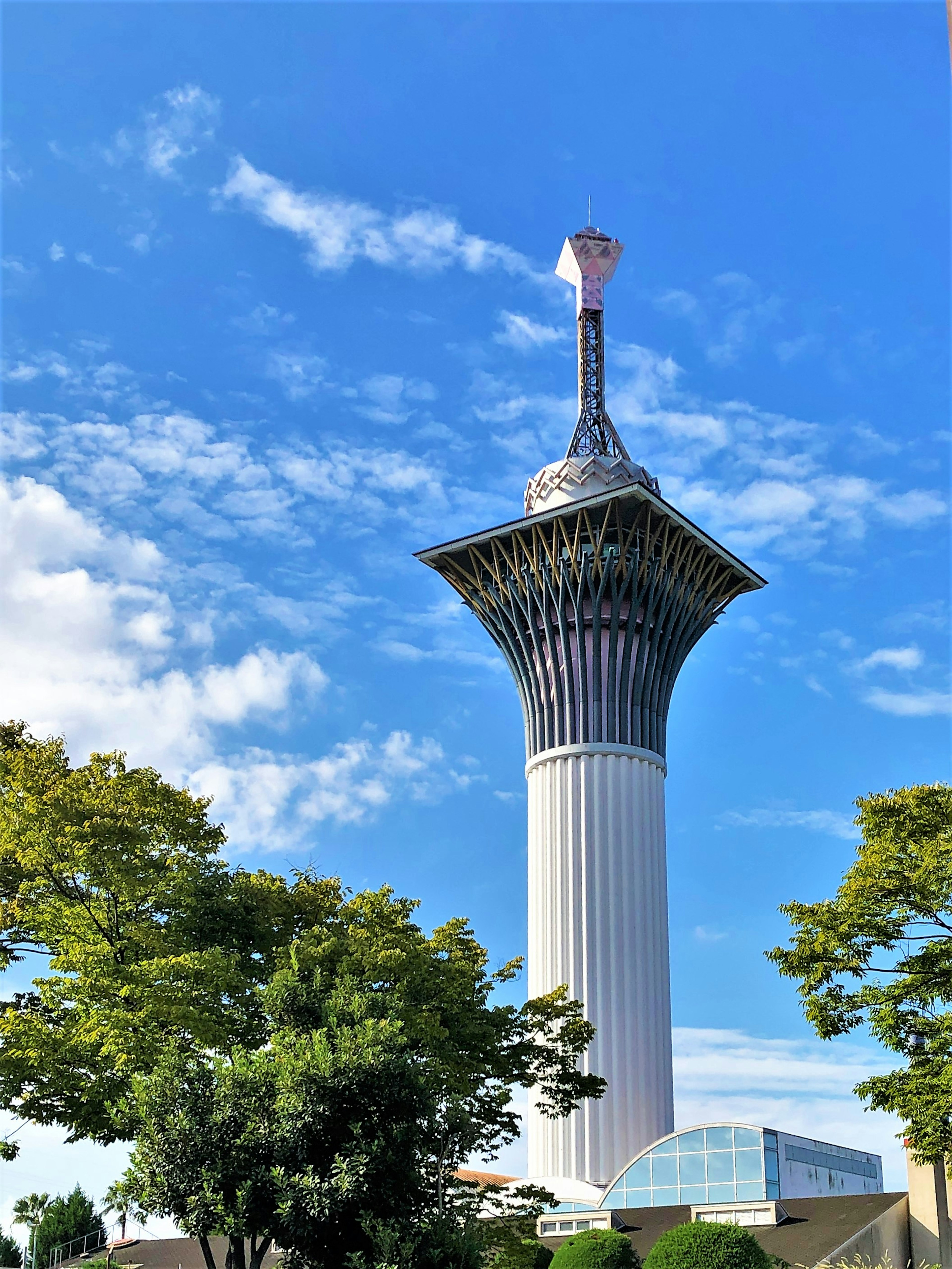 Gambar menara tinggi di bawah langit biru dengan vegetasi di sekitarnya