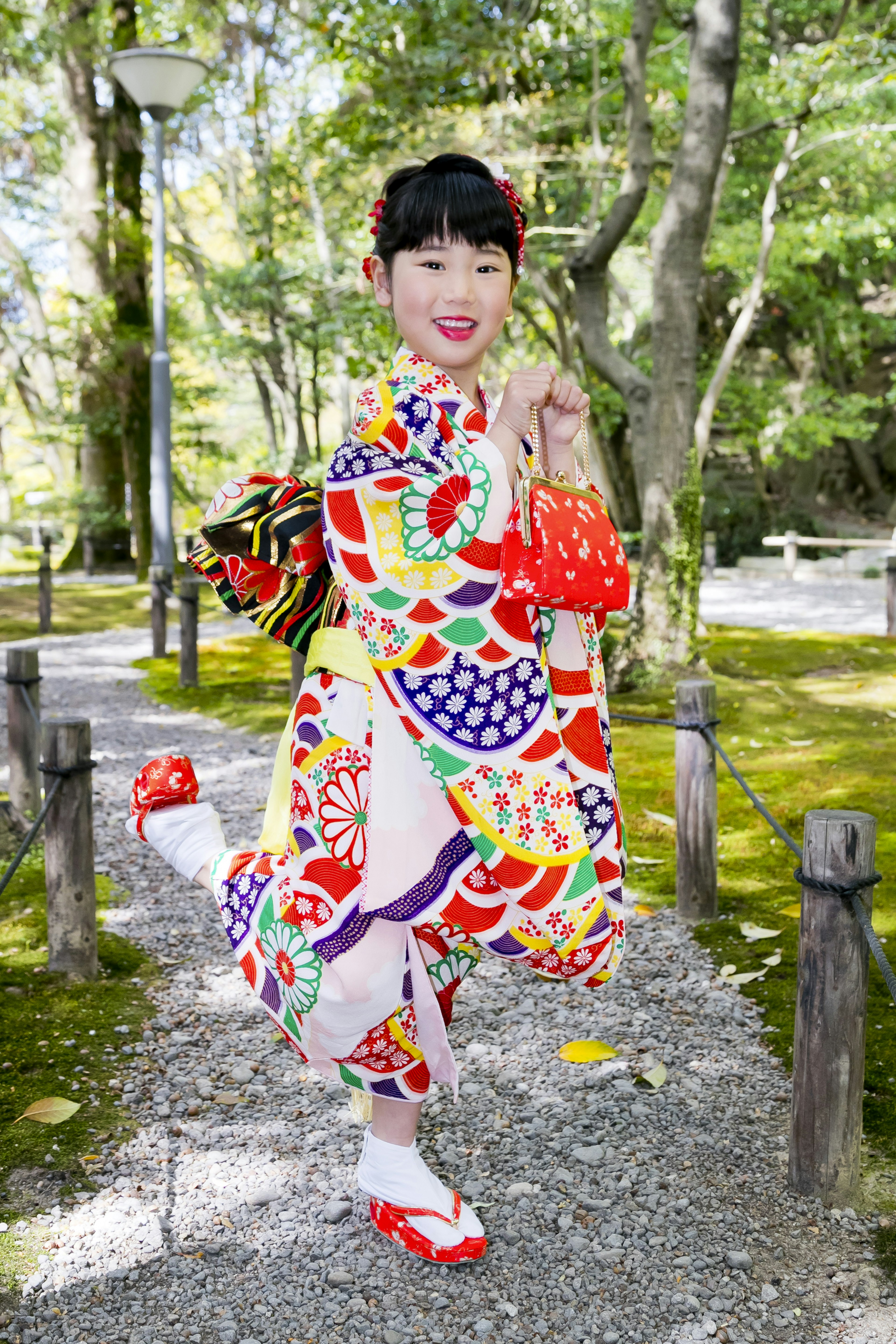 カラフルな着物を着た女性が公園の小道でポーズを取っている