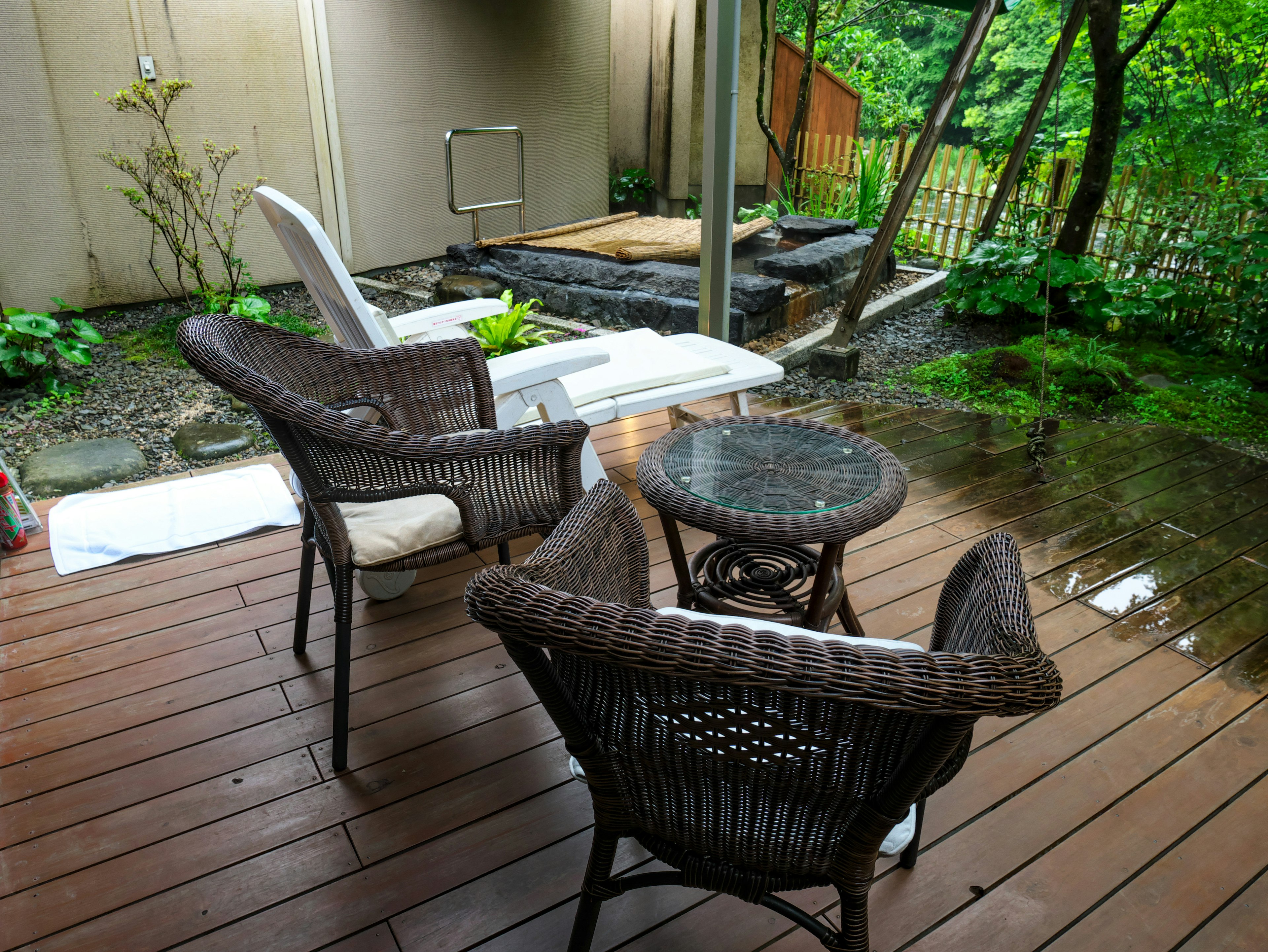 Outdoor living space featuring wicker chairs and table surrounded by lush greenery