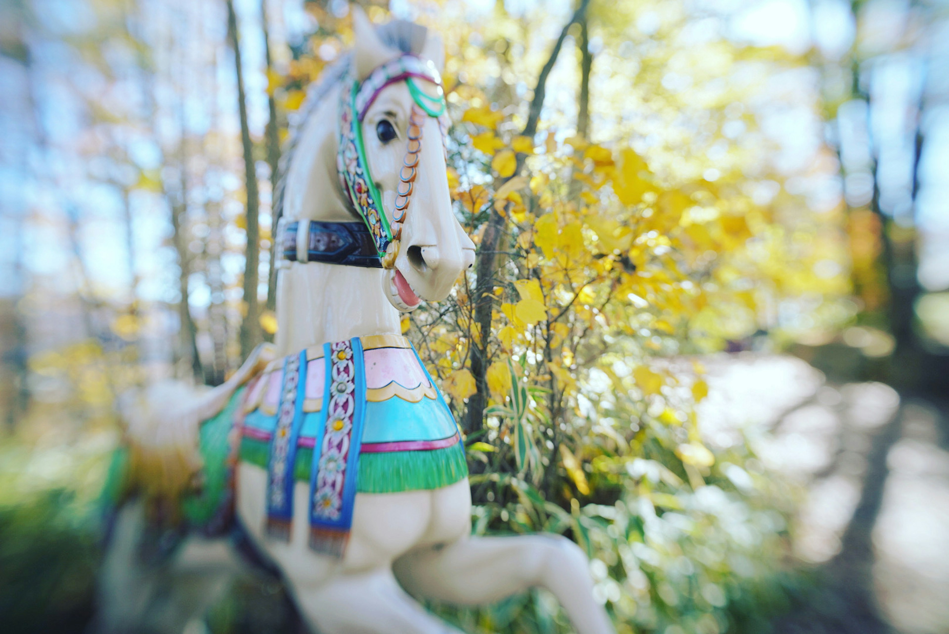 Una escultura de caballo de madera colorida rodeada de hojas amarillas de otoño