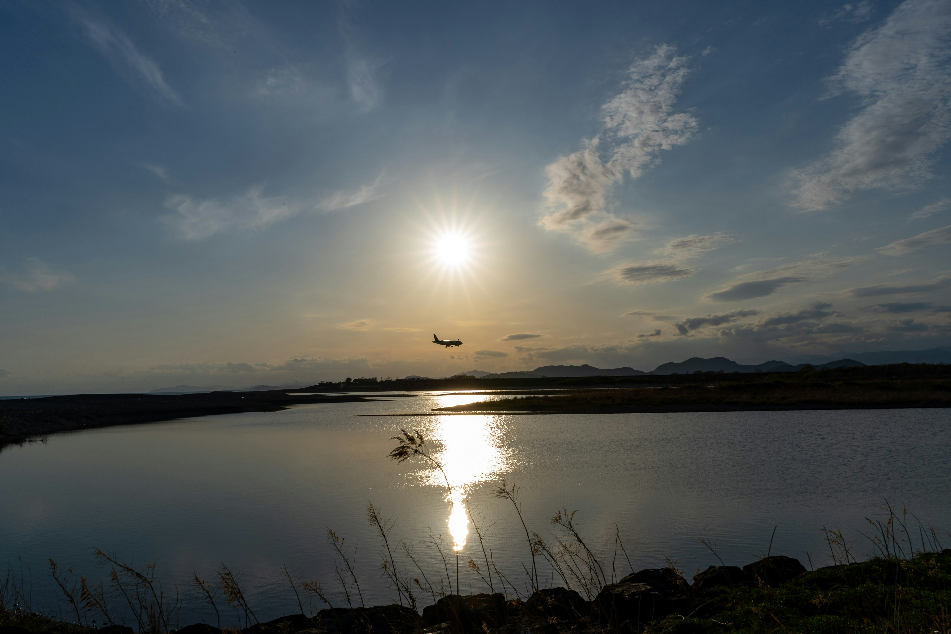 夕日が水面に映る静かな風景飛行機が空を飛んでいる