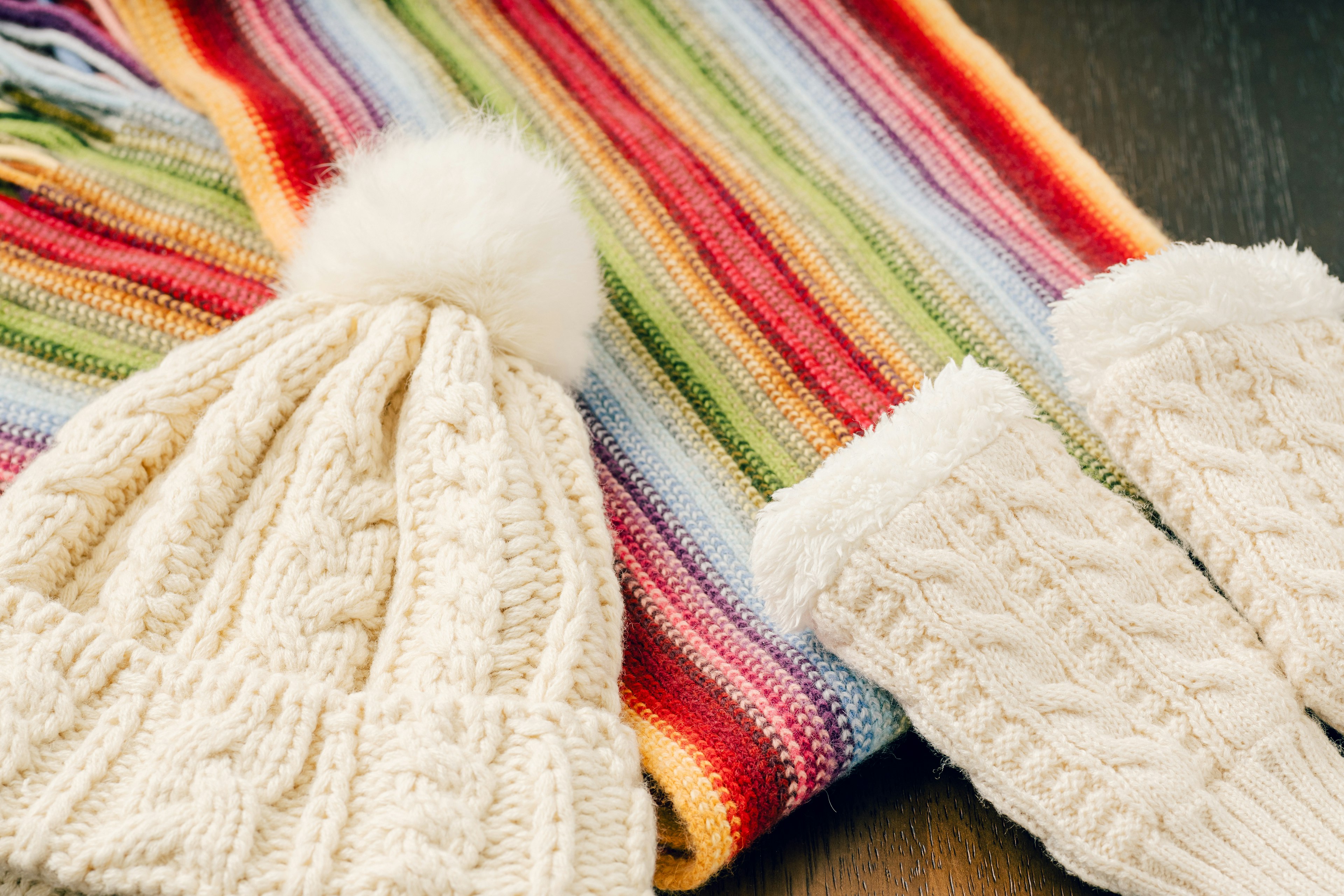 Accessori invernali con un cappello lavorato a maglia e guanti accanto a una sciarpa a righe