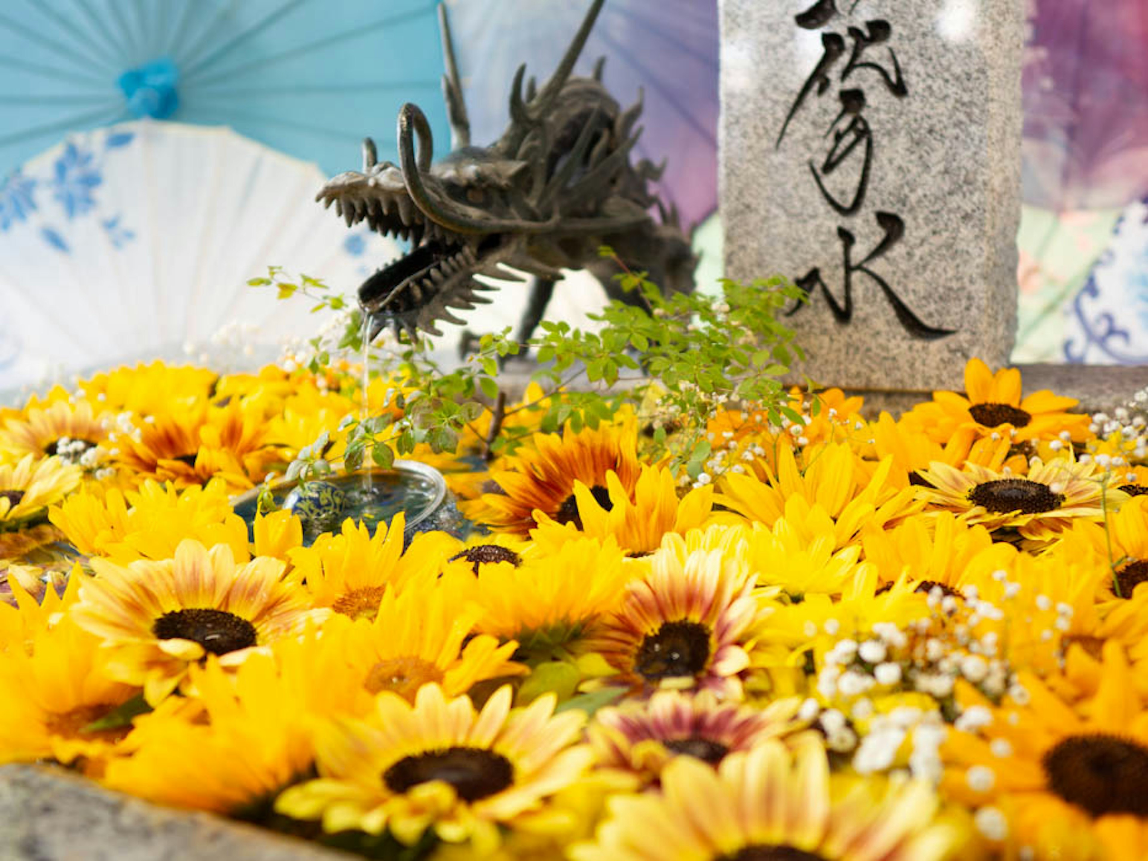 A vibrant scene with sunflowers and a dragon sculpture surrounded by colorful umbrellas