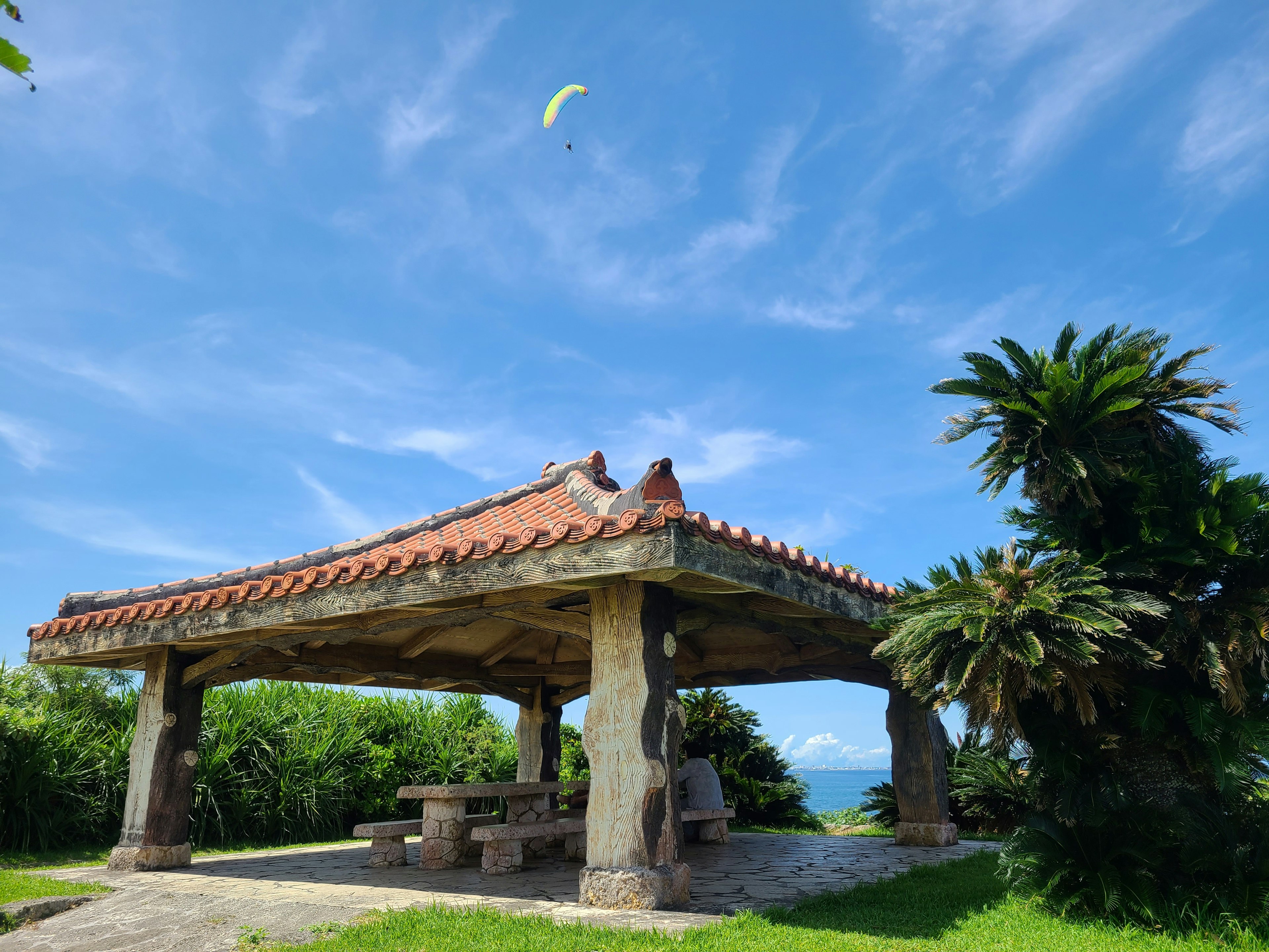 Traditionelles Pavillon mit Ziegeldach unter blauem Himmel umgeben von Grün