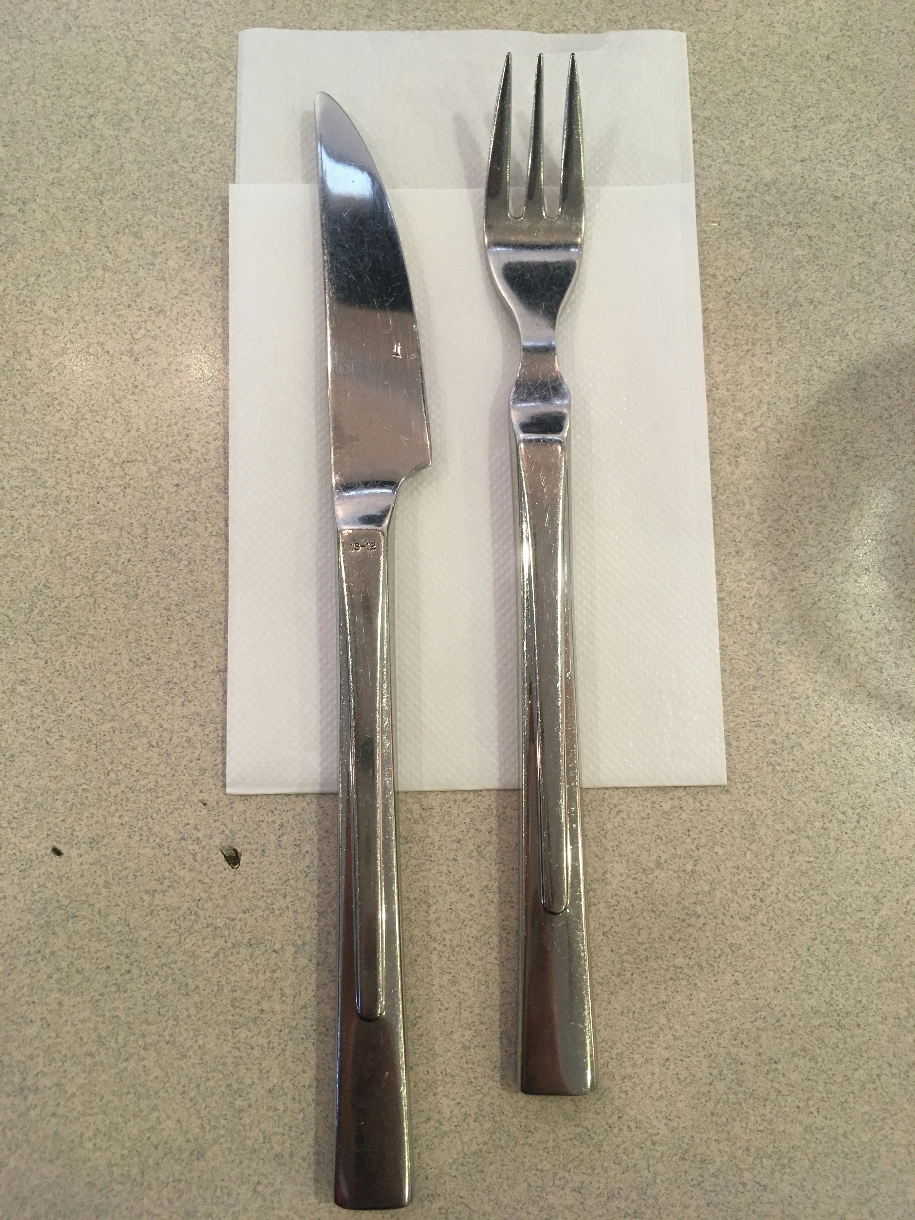 Knife and fork placed on a white napkin on a dining table