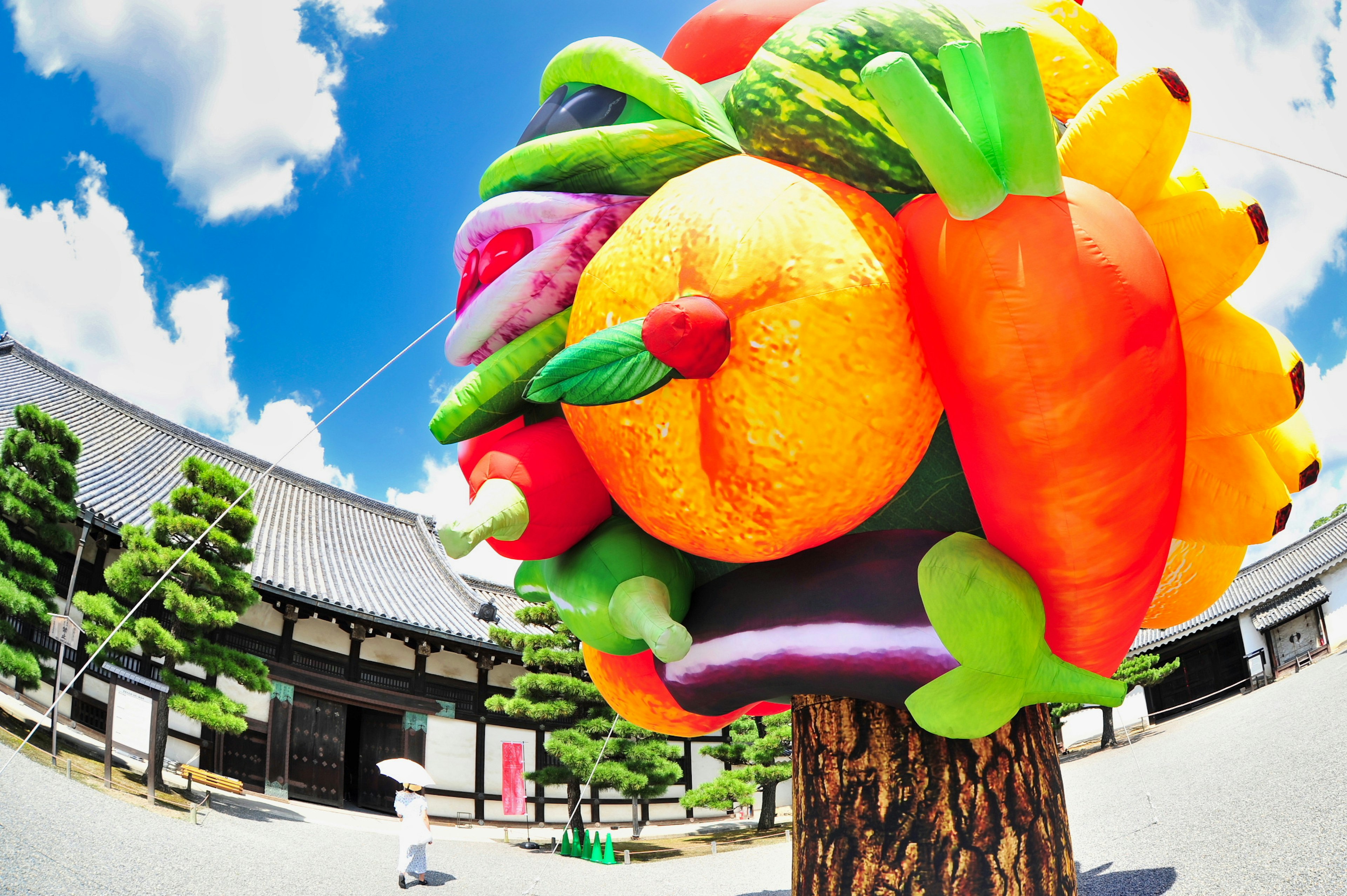 Scultura colorata di frutti e verdura su un albero sotto un cielo blu