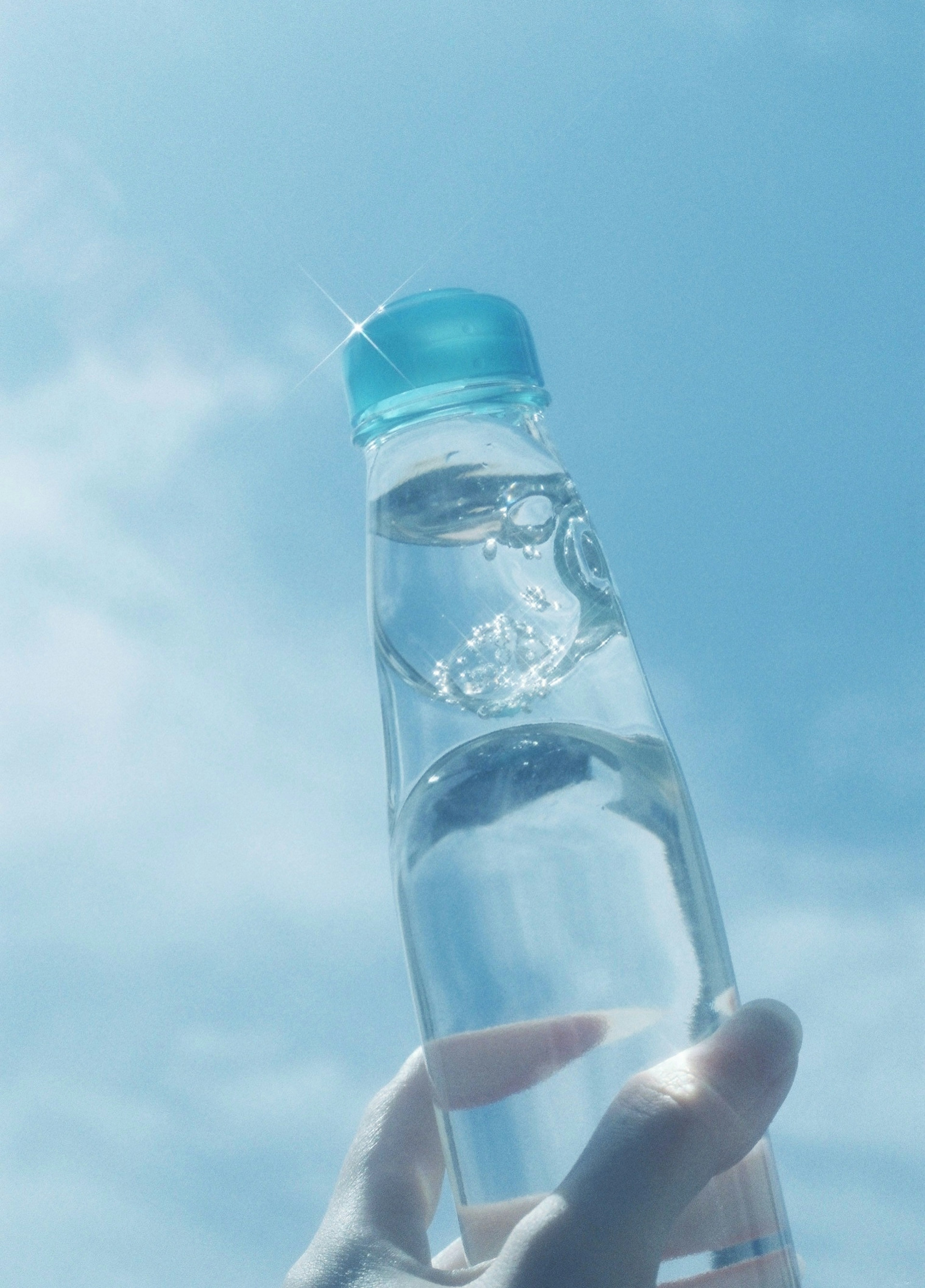 Hand holding a clear water bottle against a blue sky