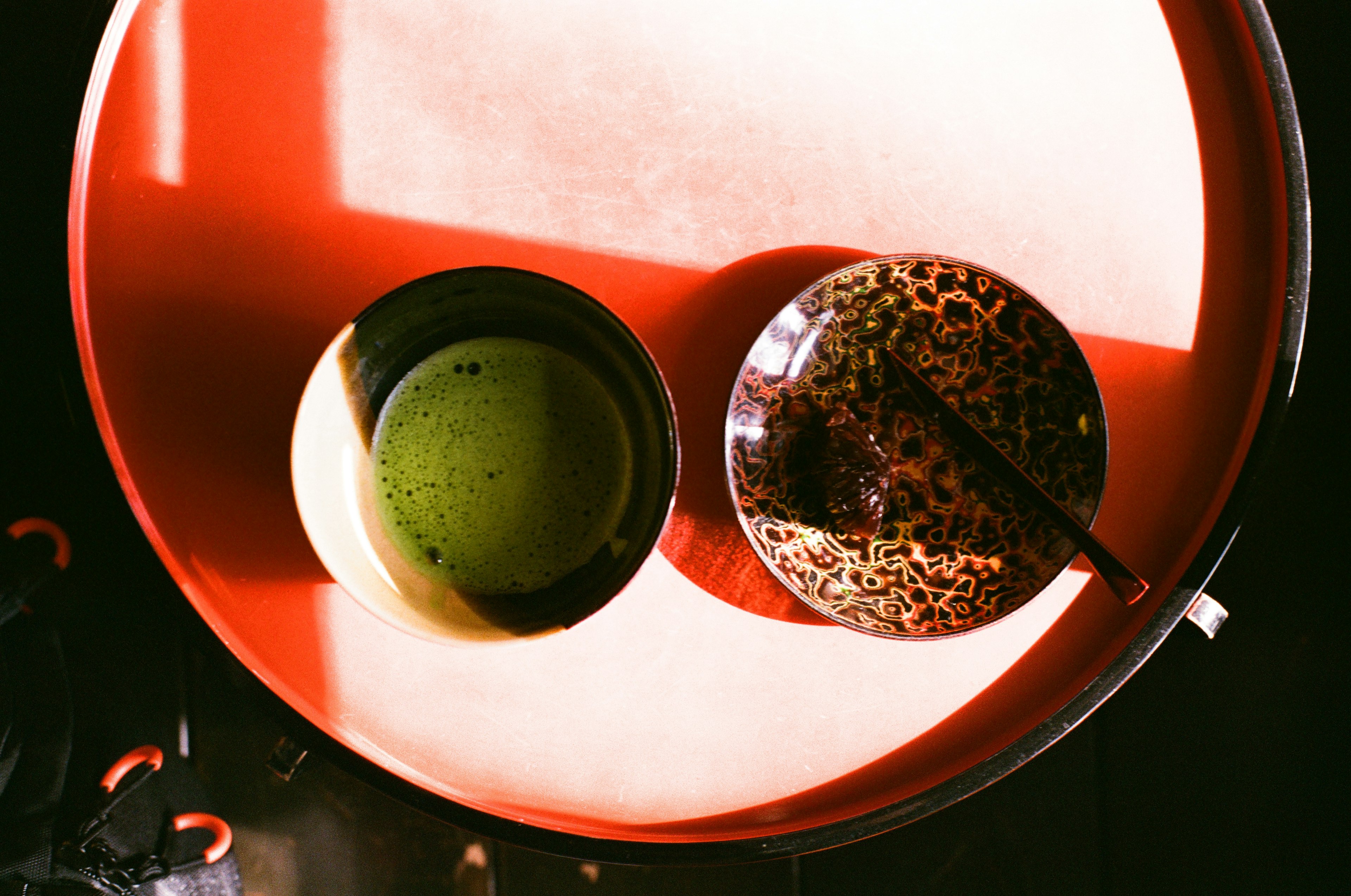 Green tea in a bowl and a patterned plate on a red tray