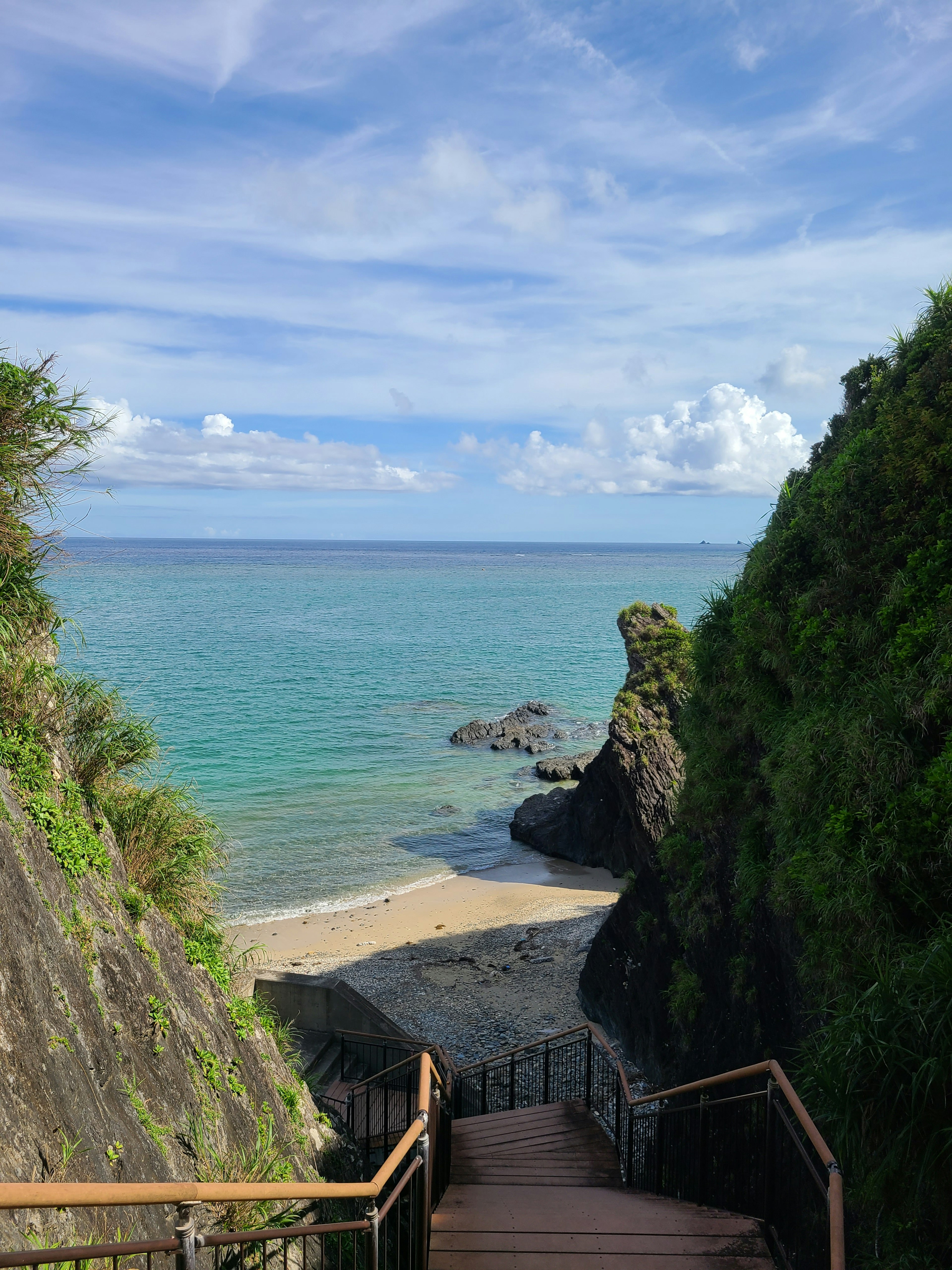 Staircase leading to a beach with turquoise water and green cliffs